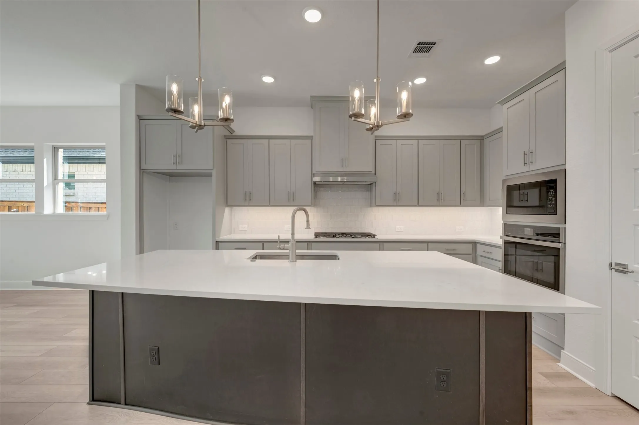 Kitchen featuring a large central island with a light-toned countertop, light gray cabinetry, stainless steel appliances, and wood-finish flooring