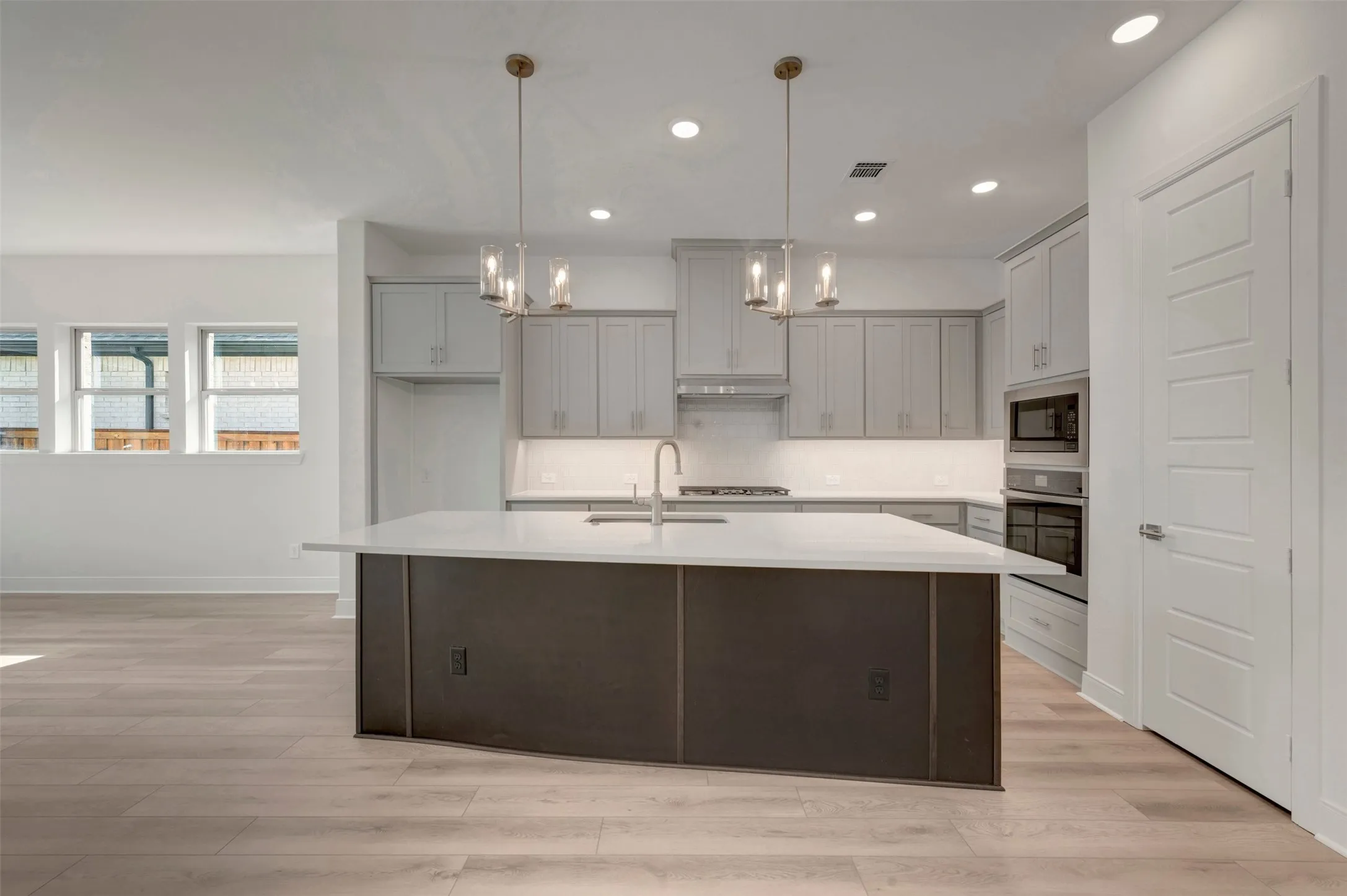 Spacious kitchen featuring a large central island with seating, pendant lighting, stainless steel appliances, and light-toned wood-finish flooring