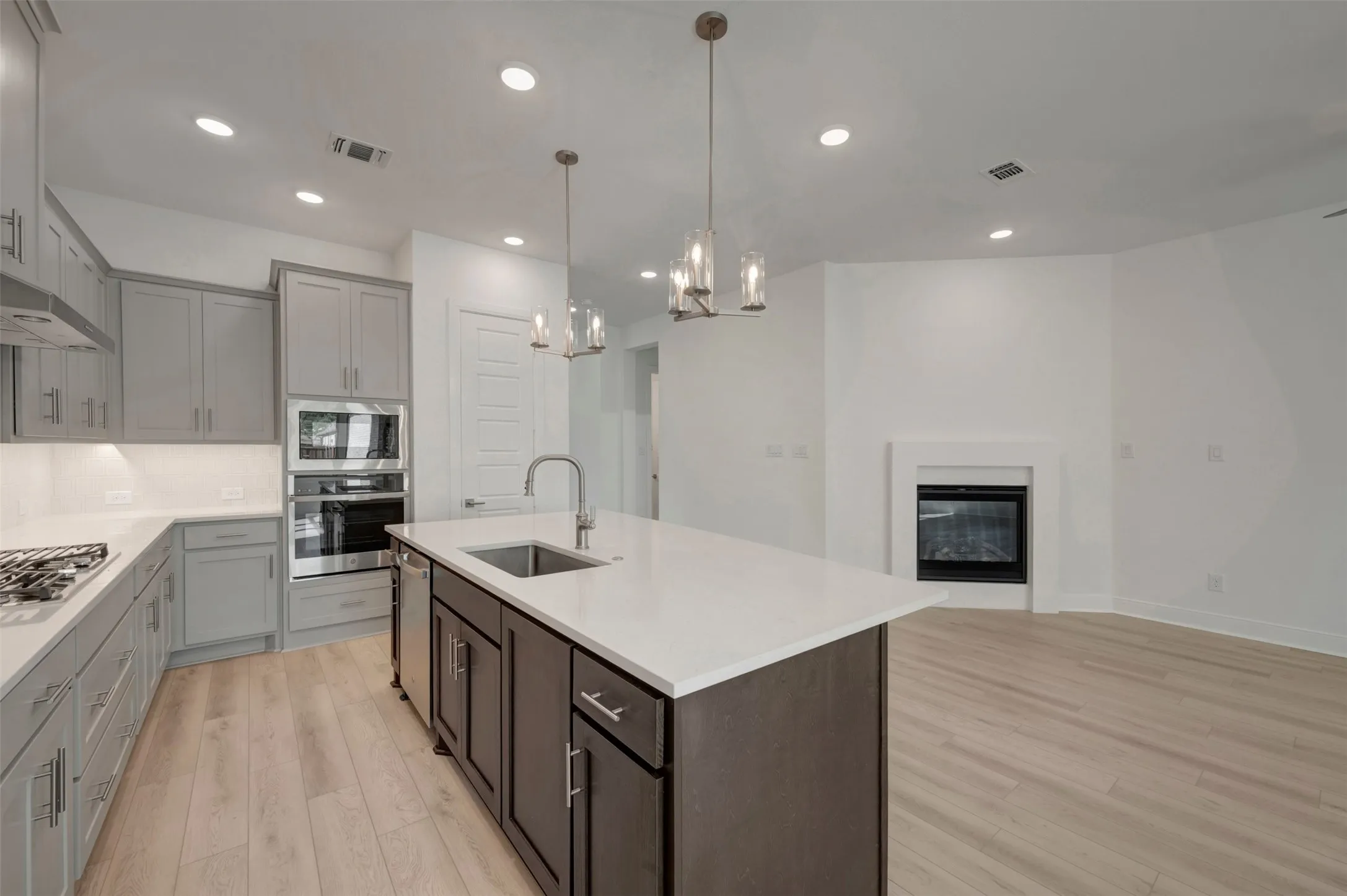 Modern kitchen featuring a central island with a sink, light-toned wood-finish flooring, recessed lighting, and a built-in oven and microwave