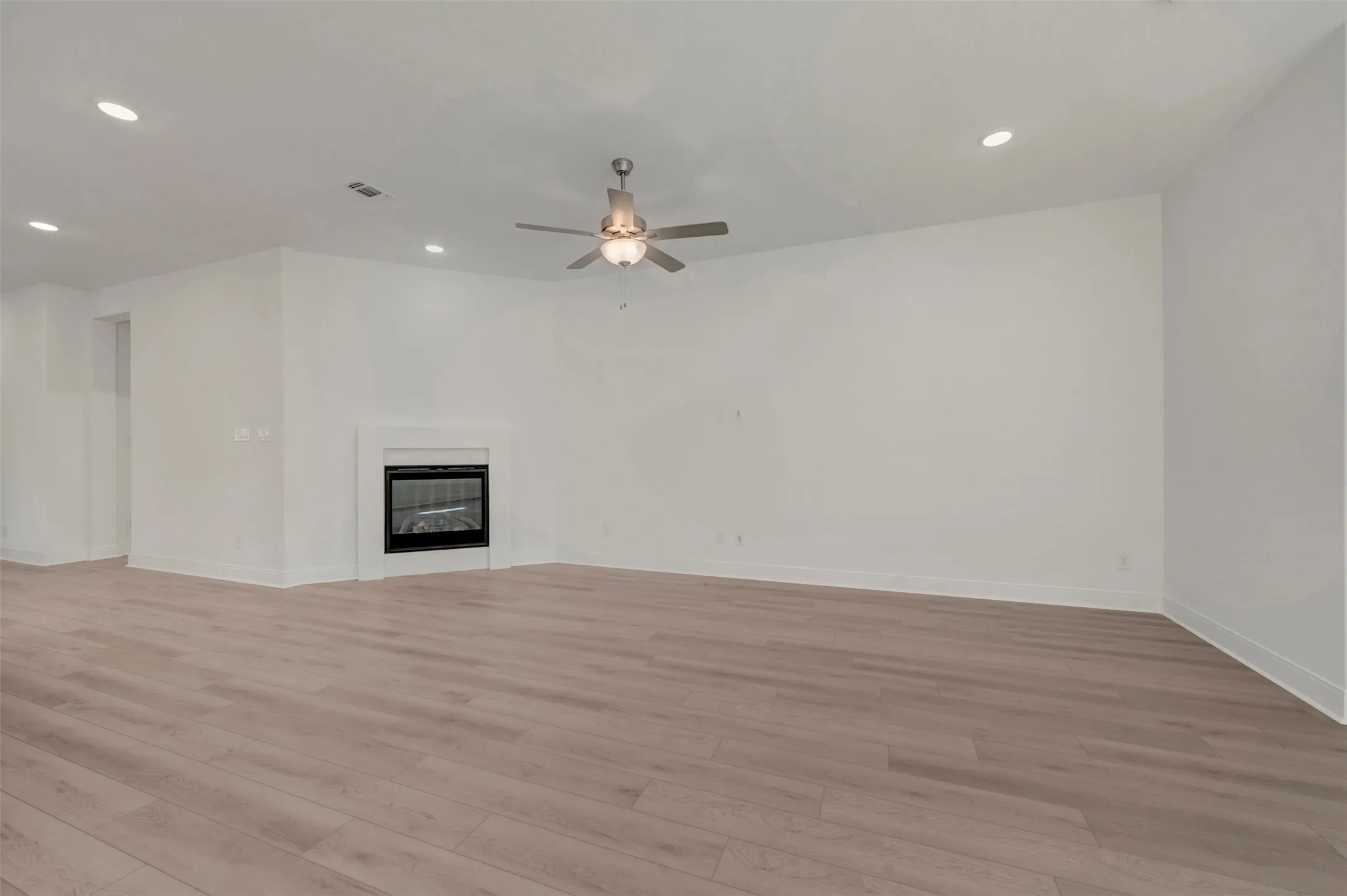 Expansive living area featuring light wood-finish flooring, a contemporary fireplace with a white surround, recessed lighting, a ceiling fan with integrated lighting, and white baseboards