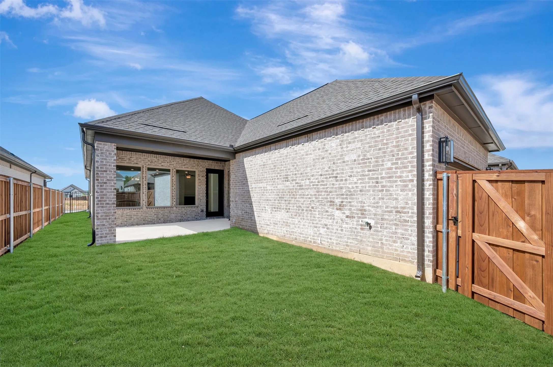 Fenced backyard with a covered patio, featuring a brick exterior and a dark asphalt shingle roof