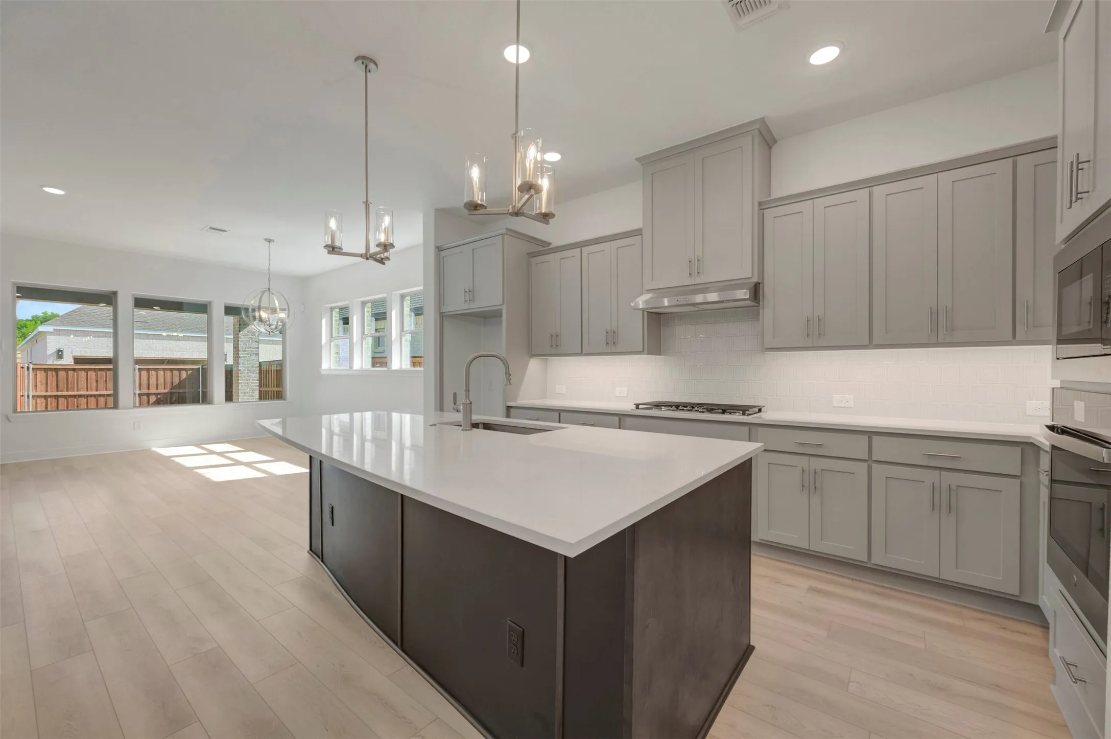 Modern kitchen featuring a large island with sink, light gray cabinetry, stainless steel appliances, and wood-finish flooring