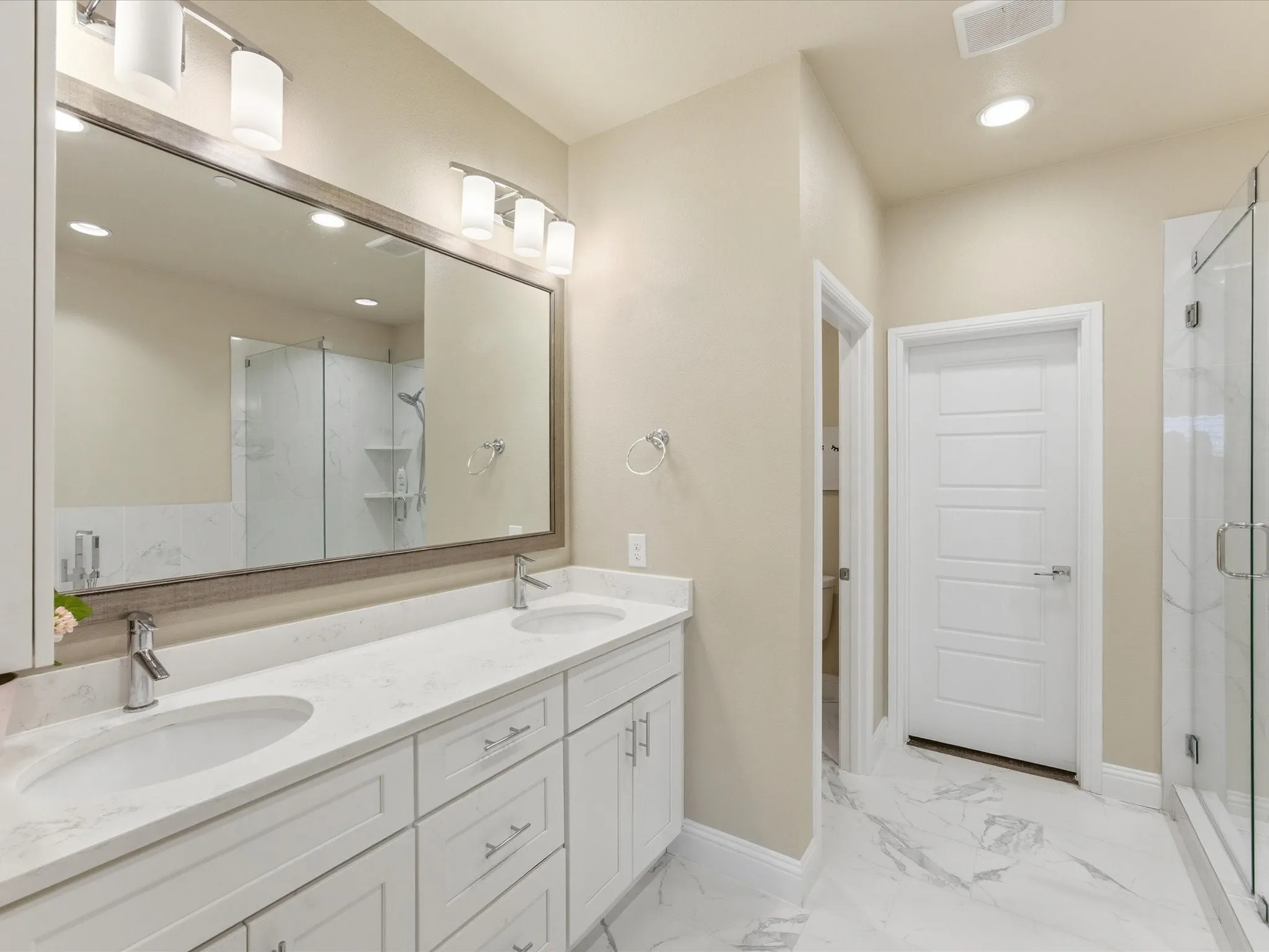 Primary bath featuring double vanity, a shower stall, recessed lighting, and light marble finish flooring