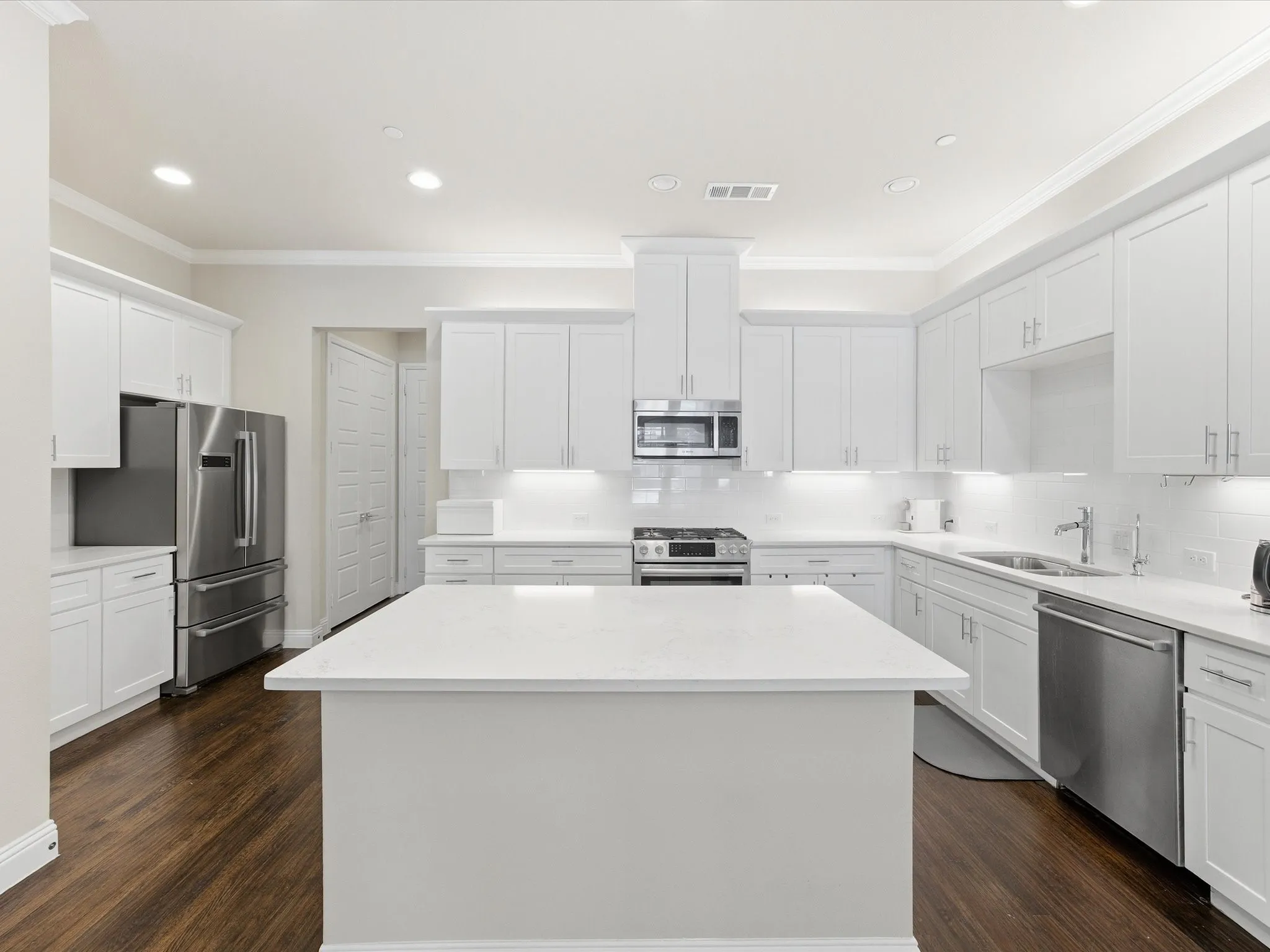 Kitchen with stainless steel appliances, a center island, white cabinetry, crown molding, and light stone countertops