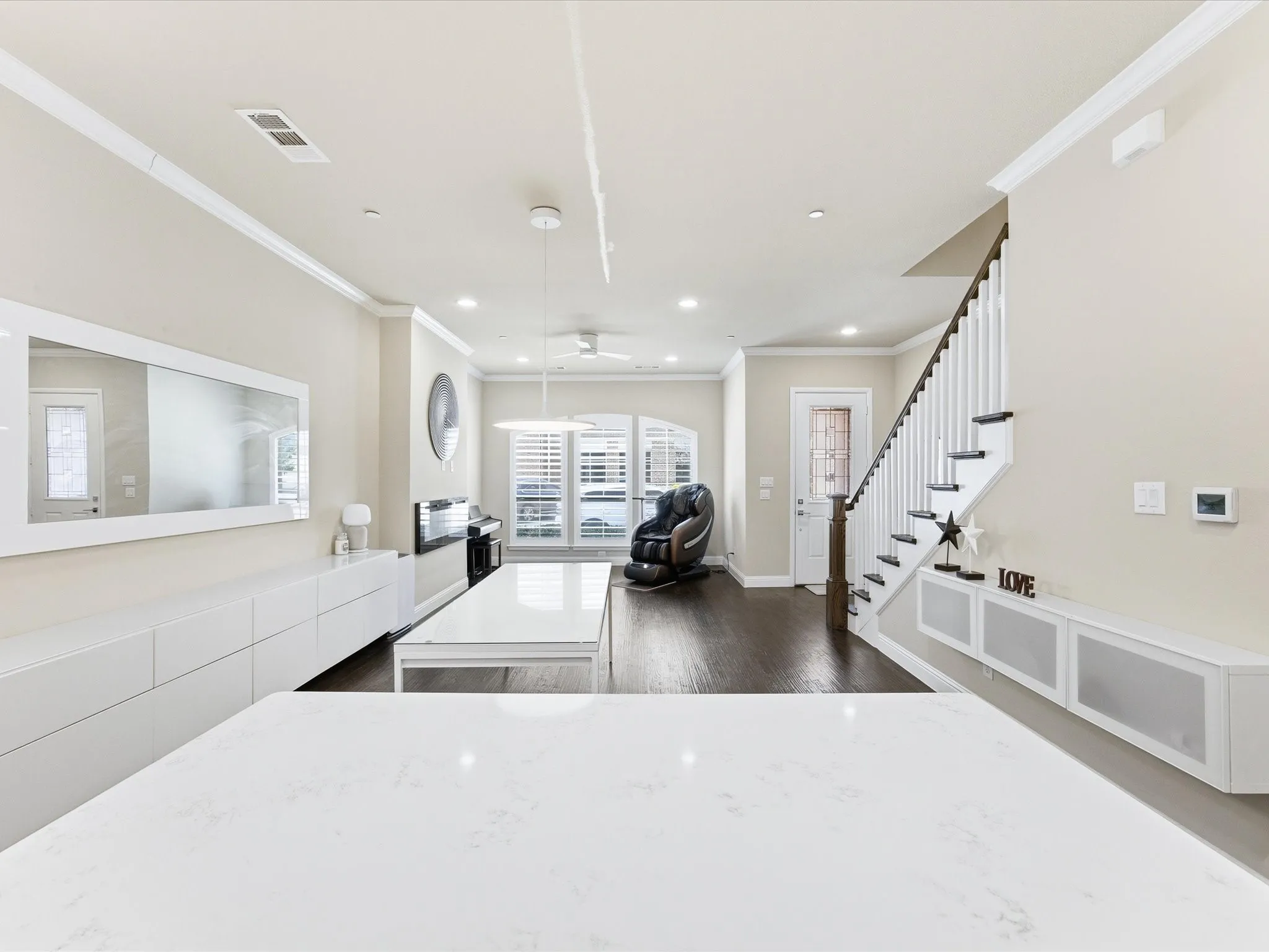 Kitchen with dark wood-type flooring, crown molding, hanging light fixtures, a ceiling fan, and light stone counters