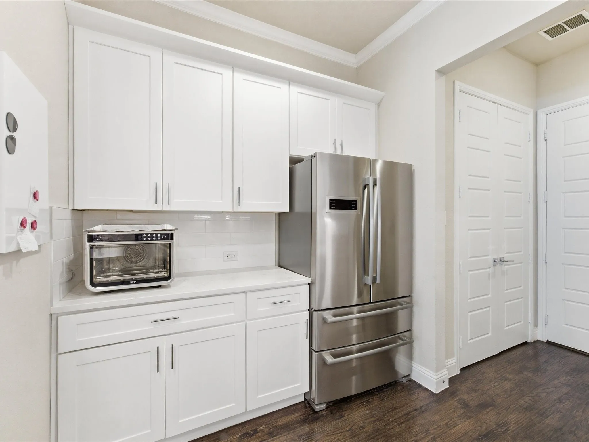 Kitchen featuring freestanding refrigerator, white cabinets, ornamental molding, tasteful backsplash, and dark wood-type flooring