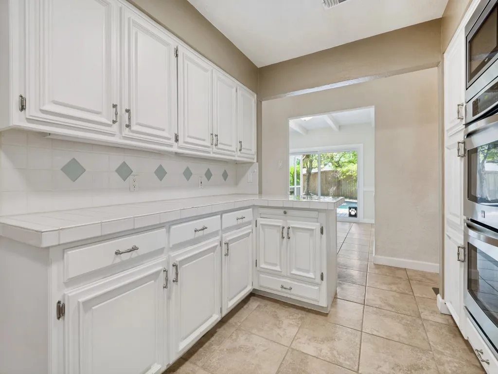 Kitchen featuring tile counters, white cabinetry, backsplash, stainless steel appliances, and light tile patterned floors