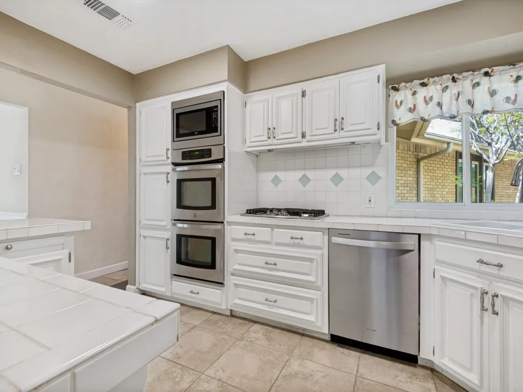 Kitchen featuring stainless steel appliances, white cabinetry, decorative backsplash, and light tile patterned floors