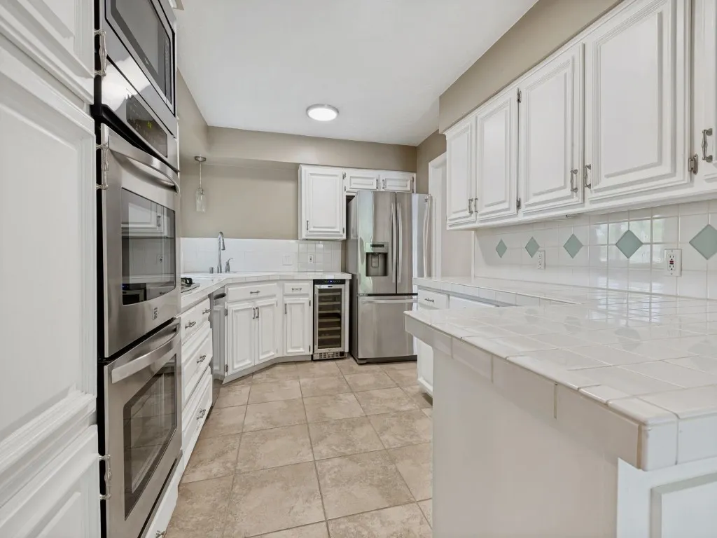 Kitchen with a peninsula, white cabinetry, stainless steel appliances, beverage cooler, and tasteful backsplash