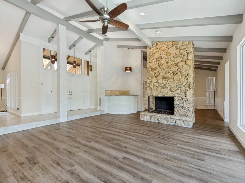 Living room with lofted ceiling, a ceiling fan, light wood-style flooring, and a stone fireplace