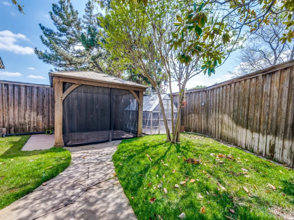 Fenced backyard featuring a gazebo and green house