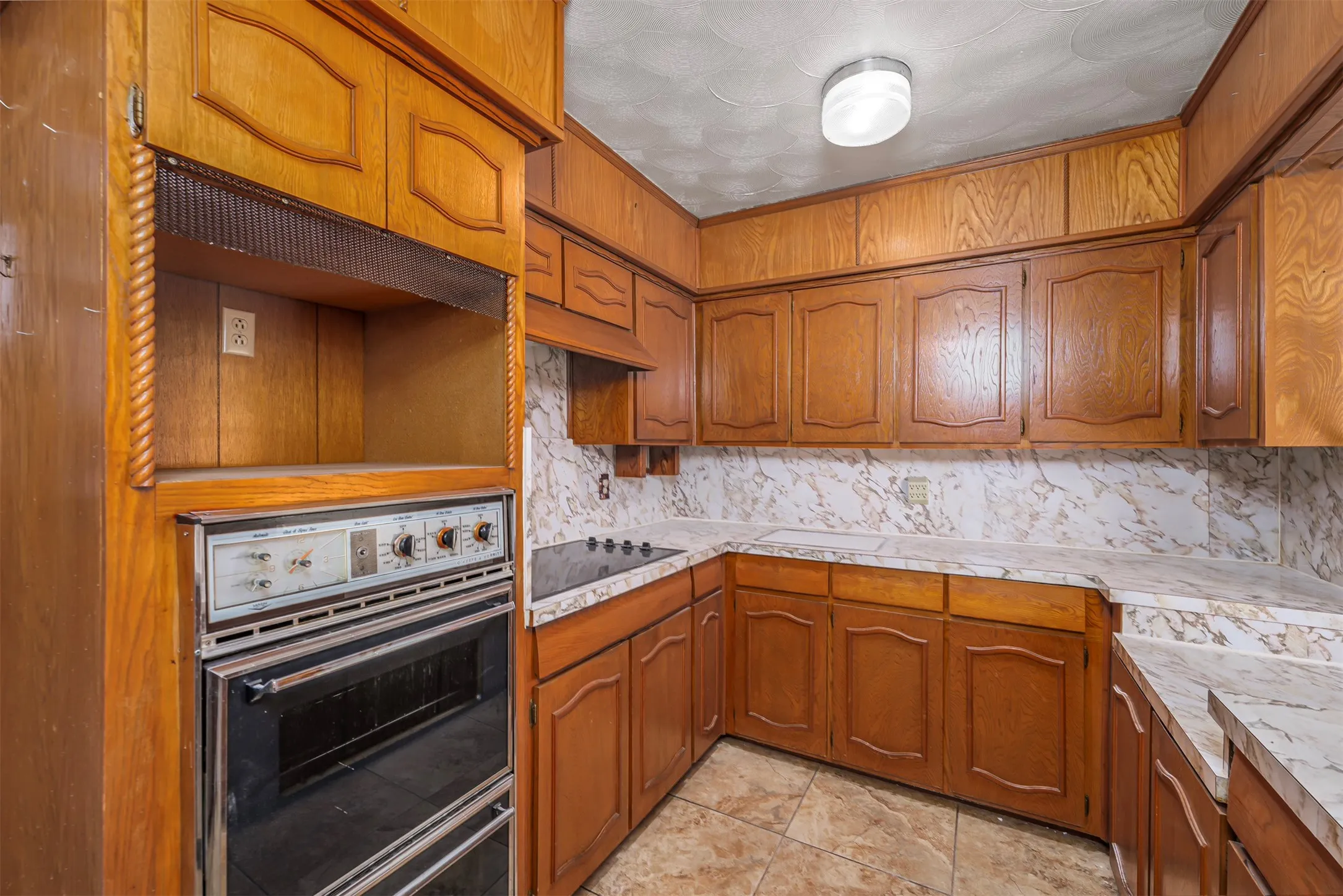 Kitchen featuring wood finish cabinets, light countertops, decorative backsplash, black electric stovetop, and ornamental molding