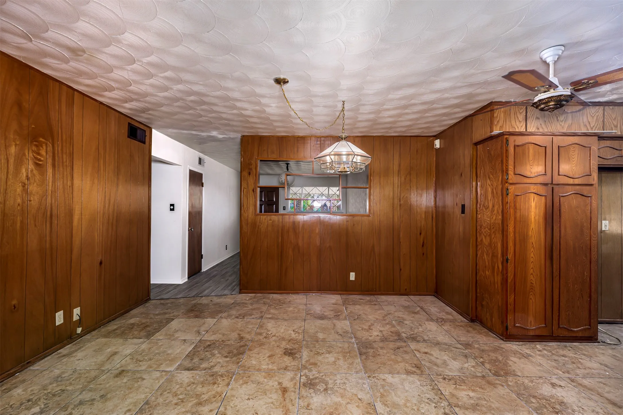 Unfurnished dining area featuring wood walls, hanging lights, ceiling fan, and stone finish floors