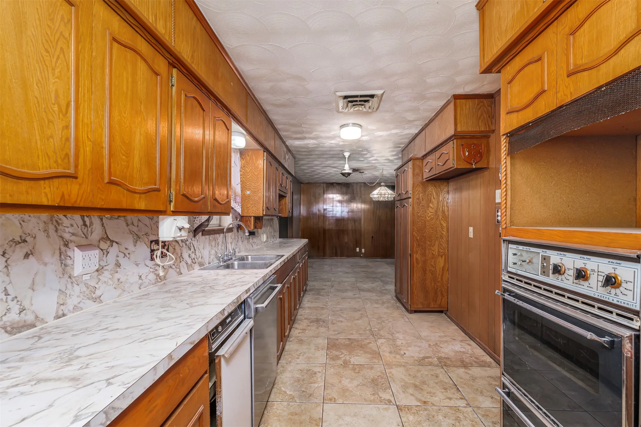 Kitchen with wood finish cabinets, light countertops, stainless steel dishwasher, wooden walls, and light tile patterned floors