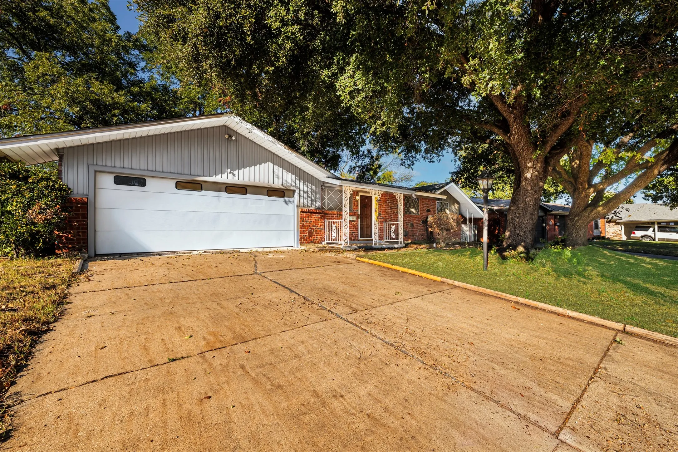 View of front of property with brick siding, a garage, driveway, a front lawn, and covered porch