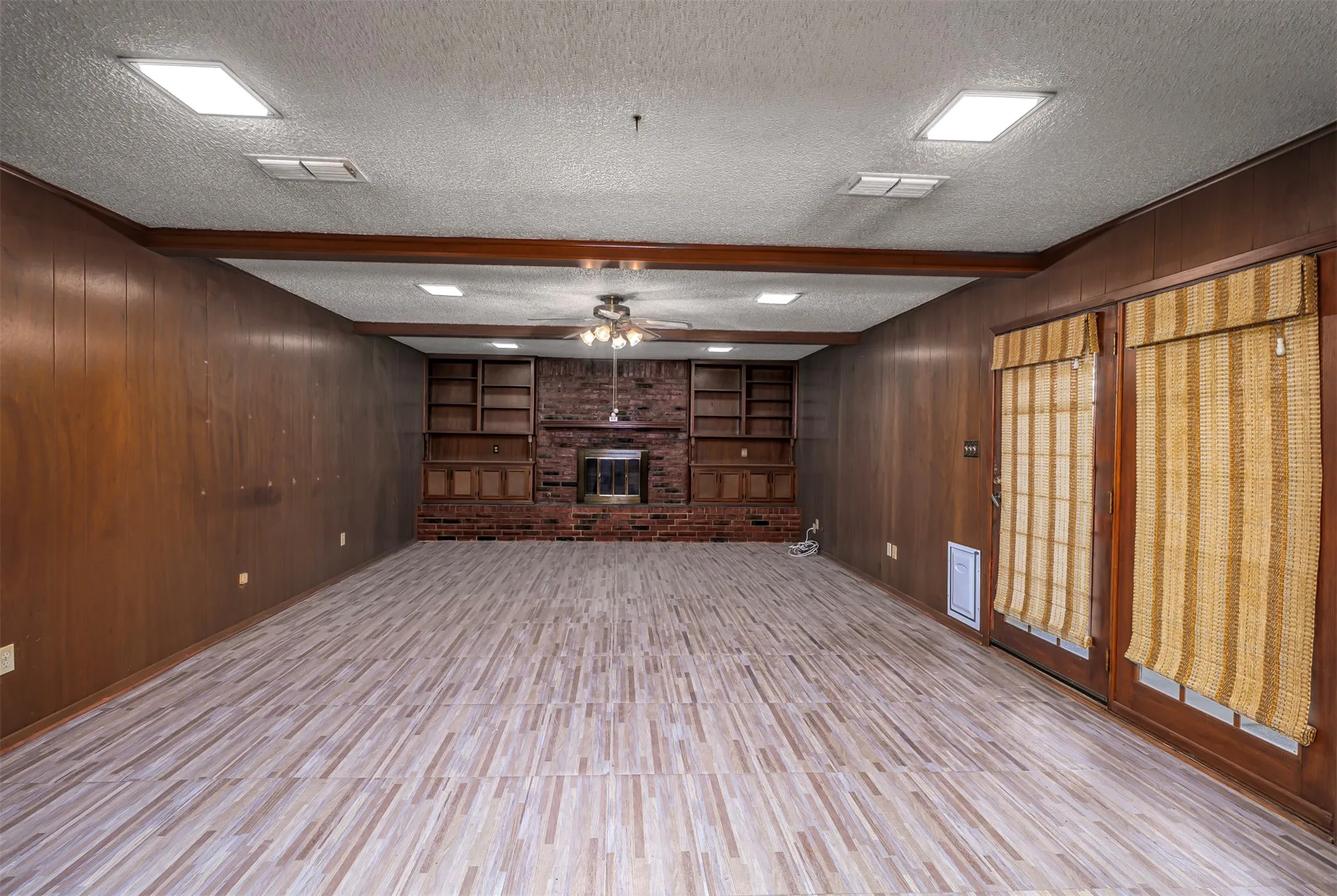 Unfurnished living room with wooden walls, beamed ceiling, ceiling fan, a textured ceiling, and built in features