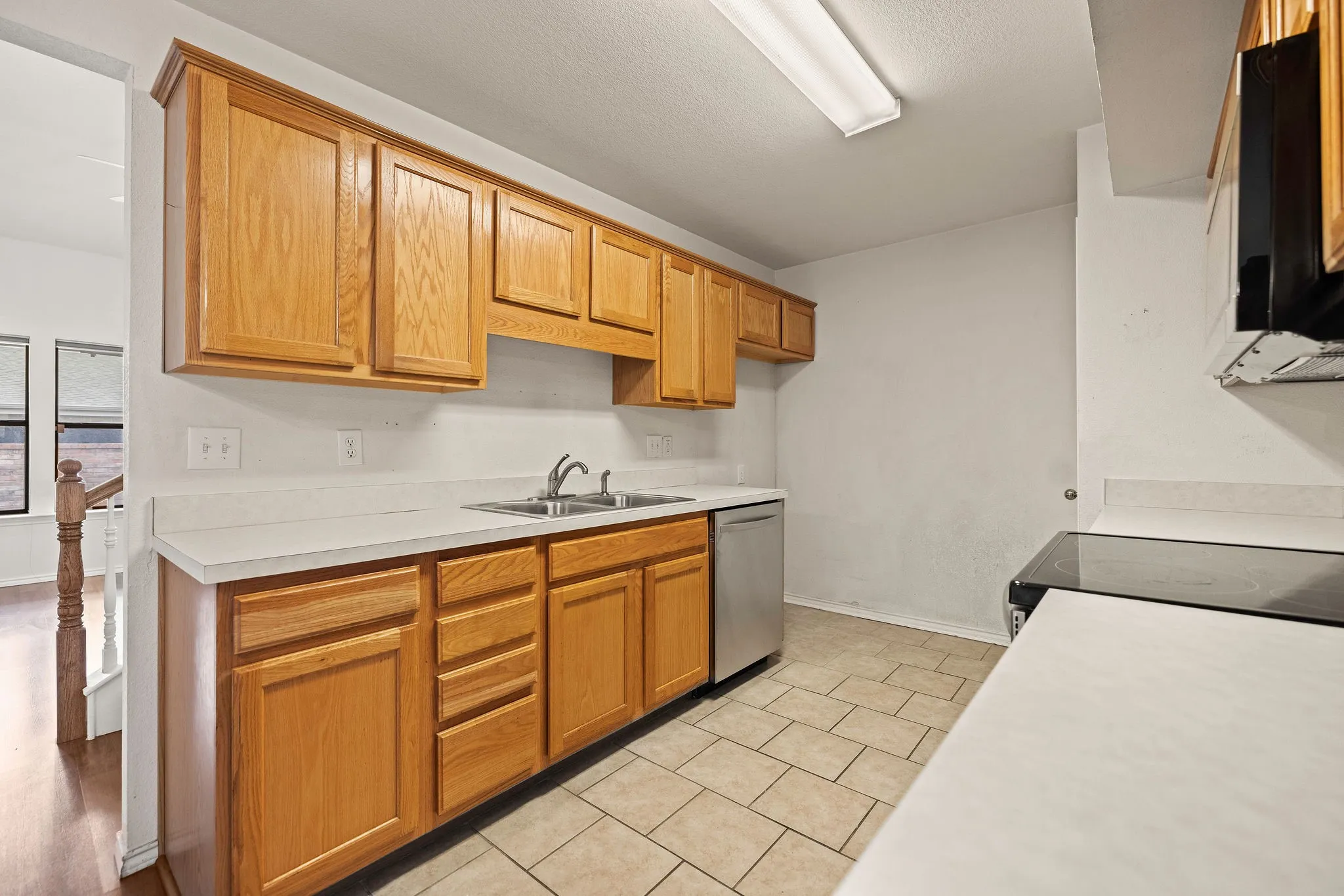 Kitchen with stainless steel dishwasher, a sink, electric range oven, light countertops, and light tile patterned floors