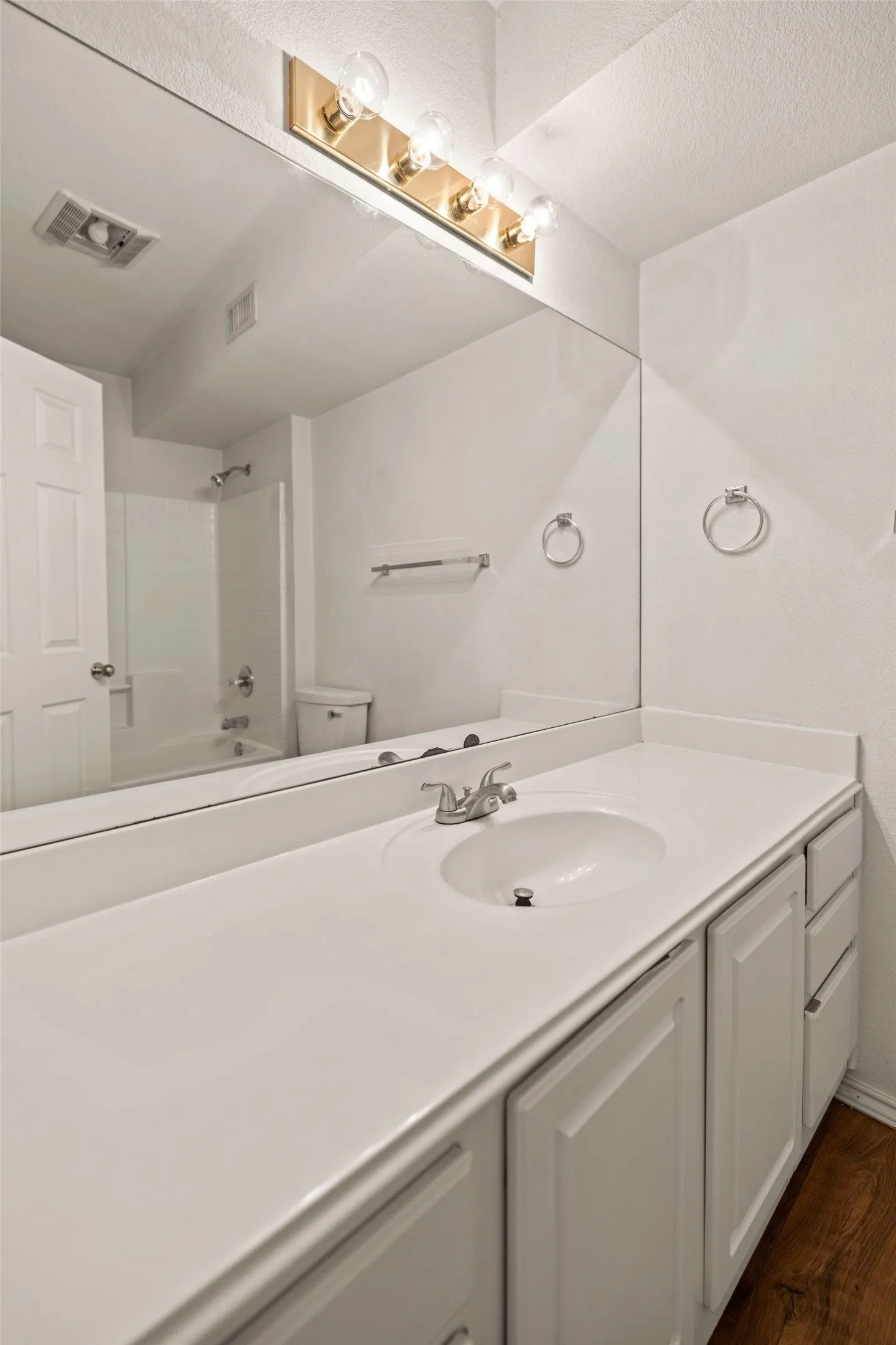 Bathroom featuring wood finished floors, shower / bath combination, vanity, and toilet