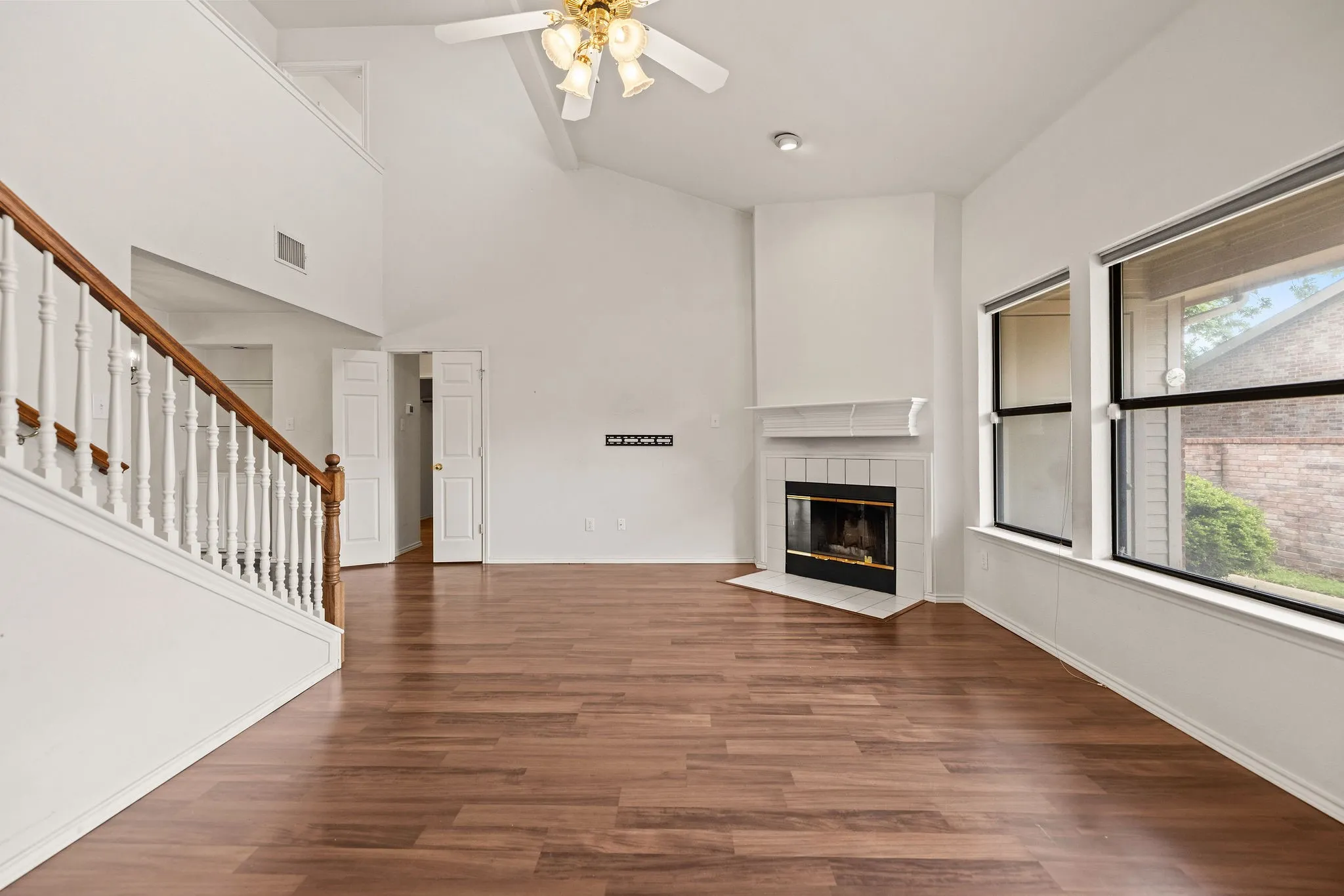 Unfurnished living room with ceiling fan, stairway, a tile fireplace, high vaulted ceiling, and wood finished floors