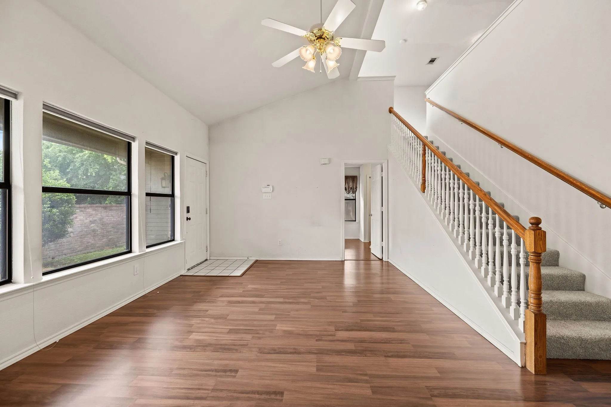Unfurnished living room with high vaulted ceiling, wood finished floors, a ceiling fan, and stairway