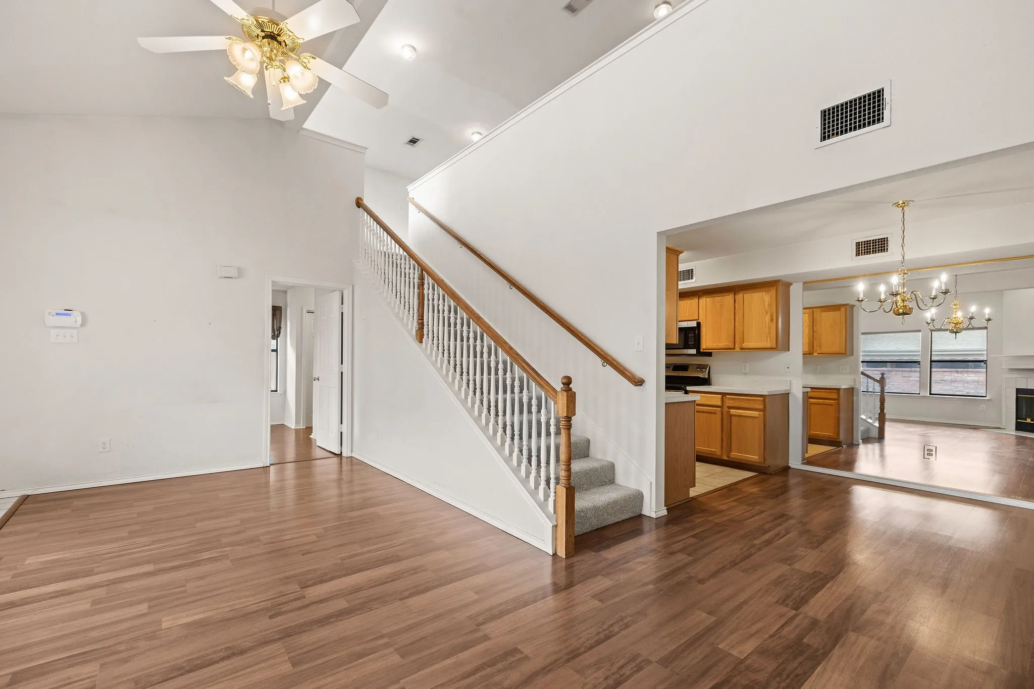 Unfurnished living room with a towering ceiling, stairs, a chandelier, wood finished floors, and a ceiling fan