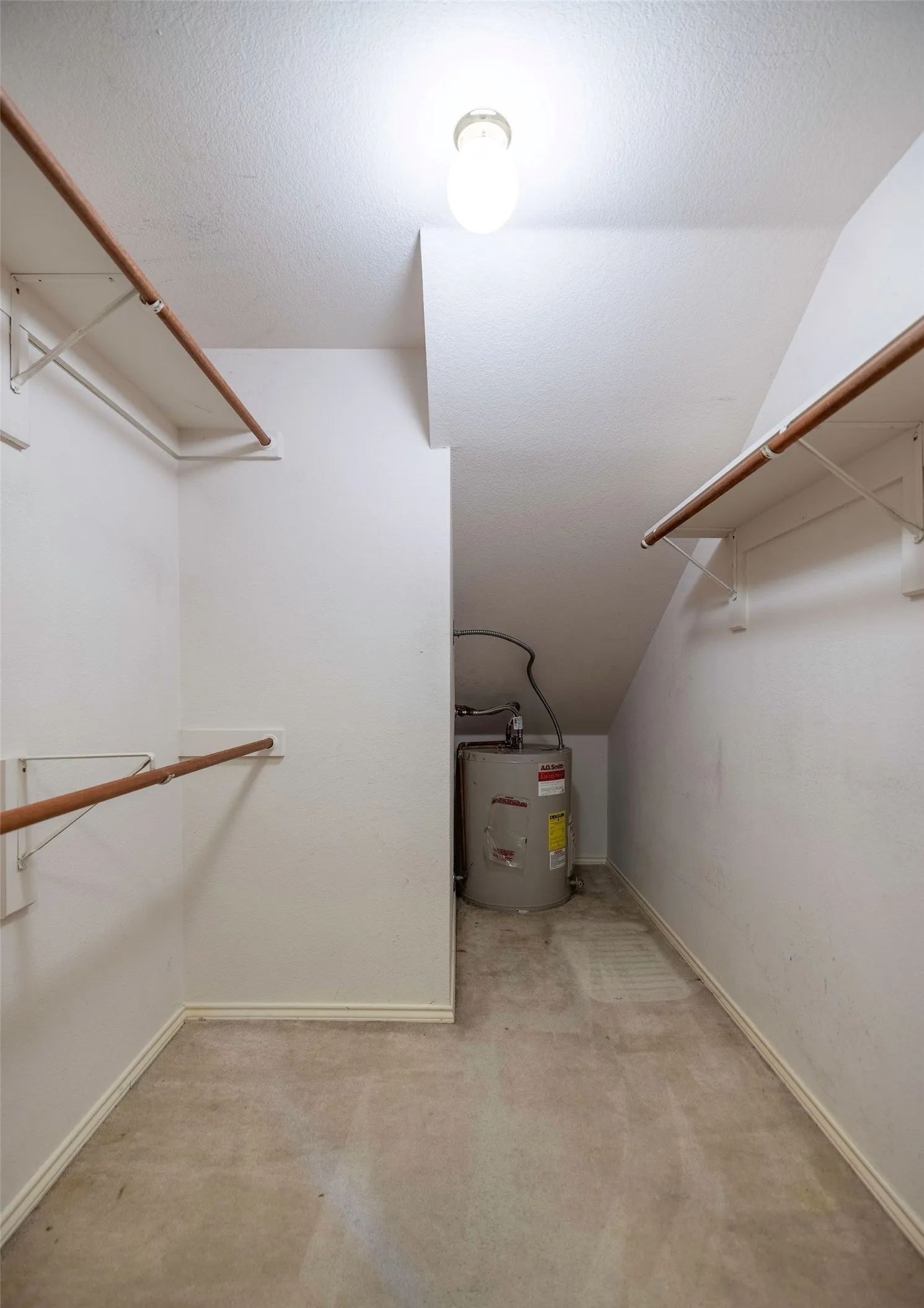 Spacious closet featuring electric water heater, carpet flooring, and vaulted ceiling