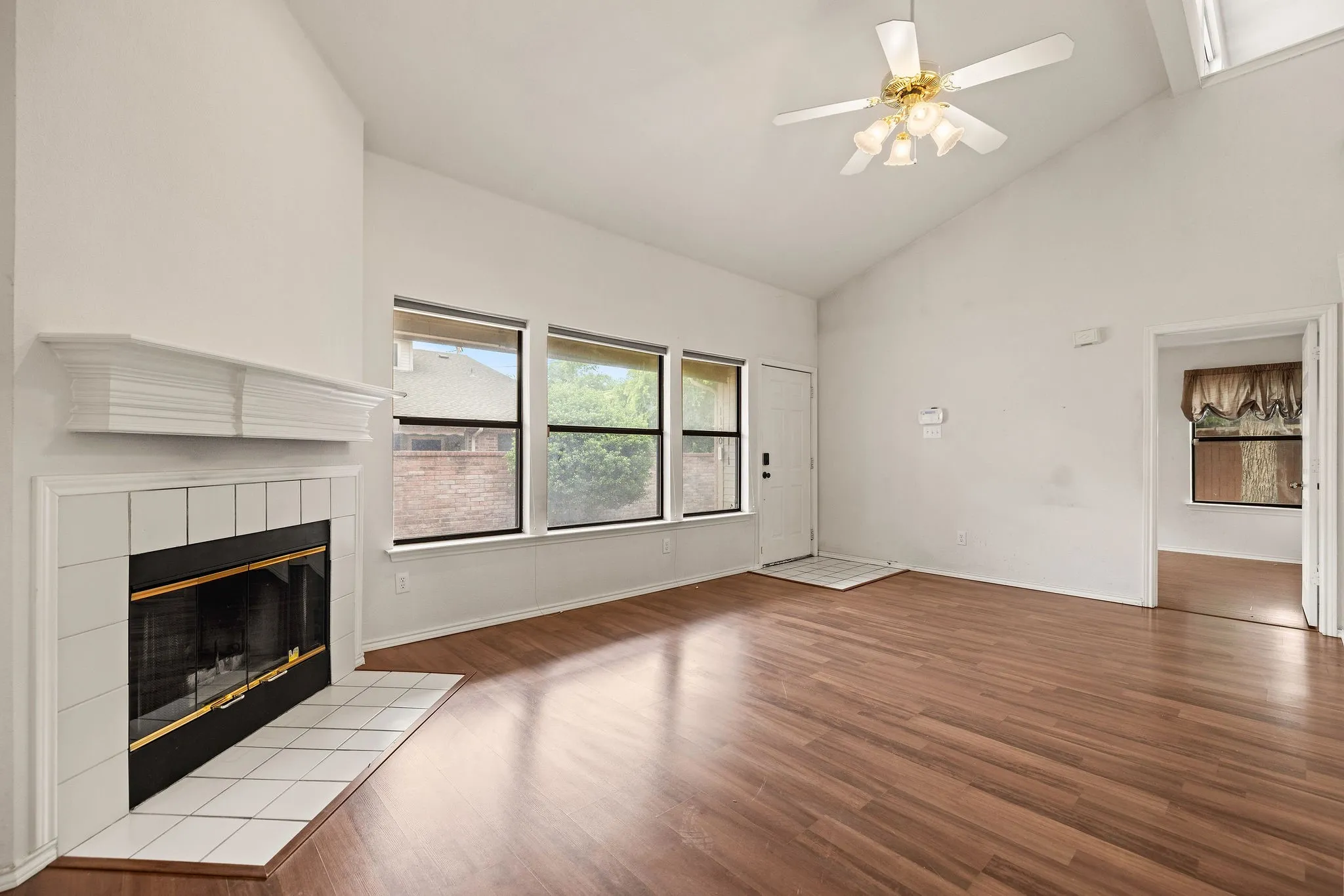 Unfurnished living room with a fireplace, high vaulted ceiling, wood finished floors, ceiling fan, and baseboards