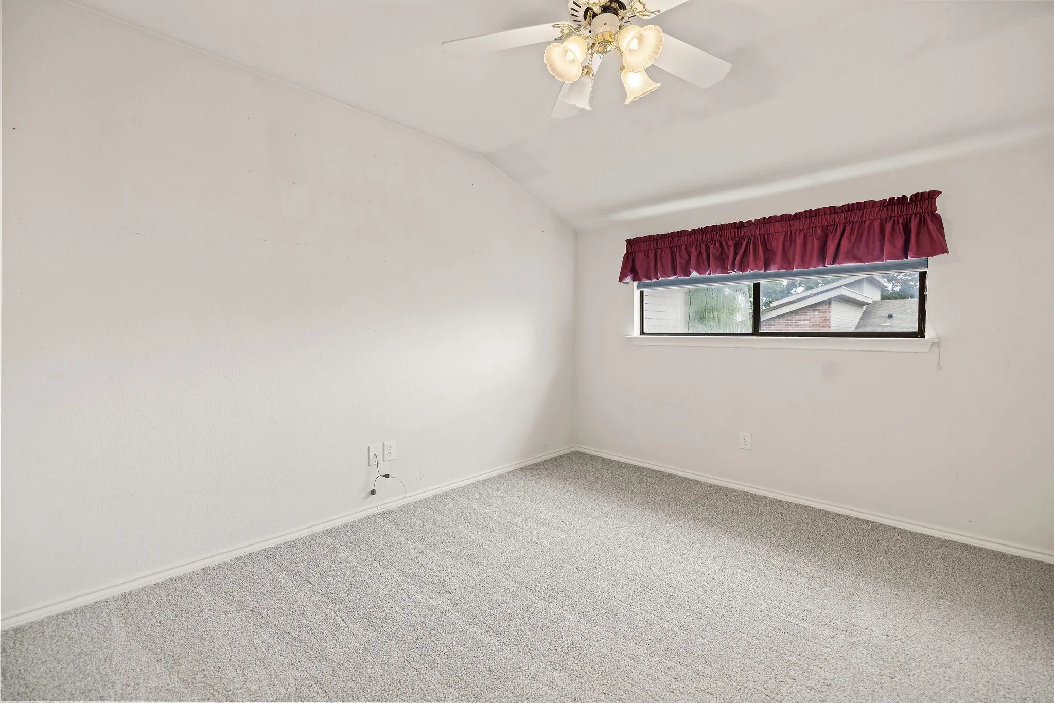Carpeted empty room with vaulted ceiling, baseboards, and a ceiling fan