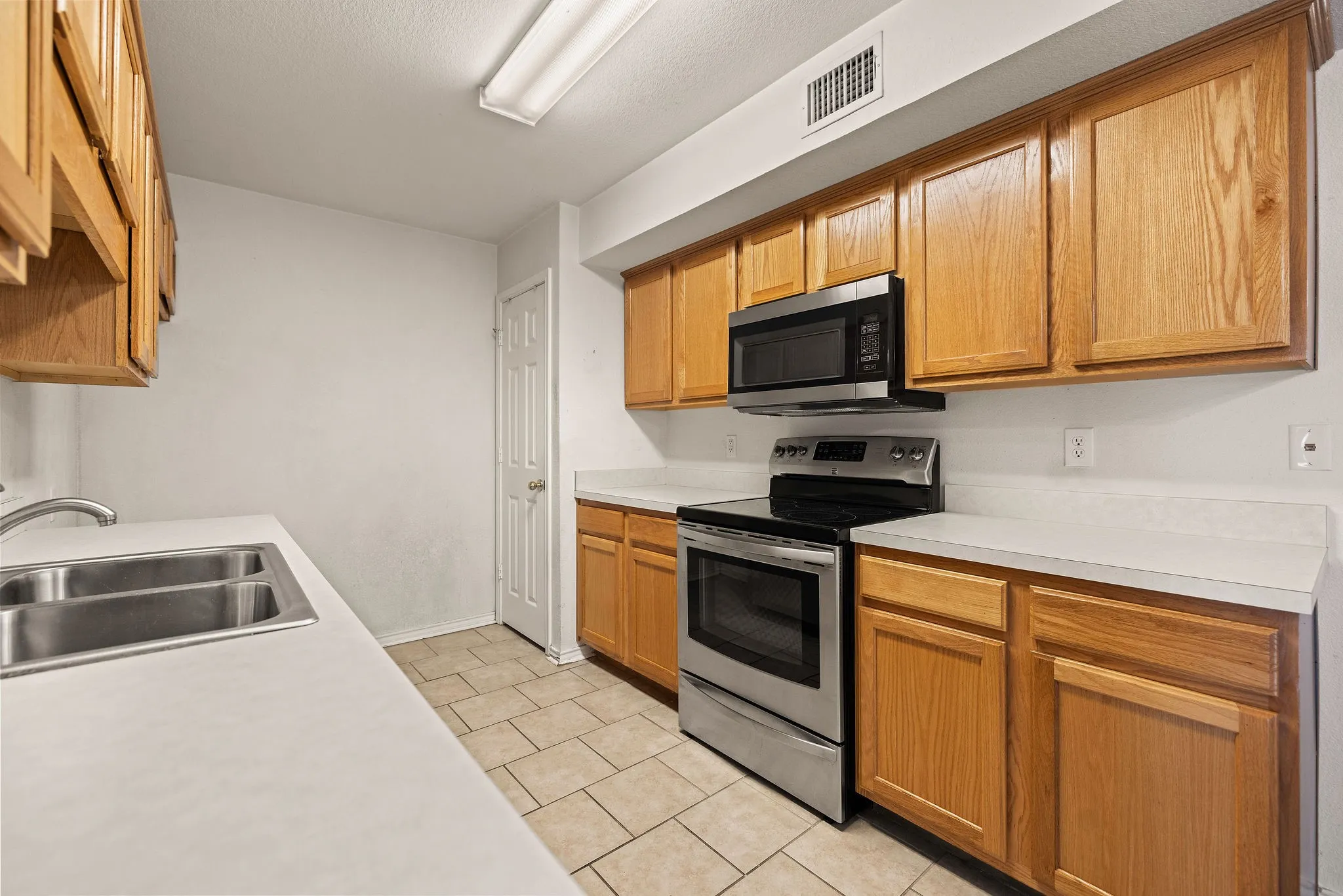 Kitchen with appliances with stainless steel finishes, a sink, light countertops, and light tile patterned flooring