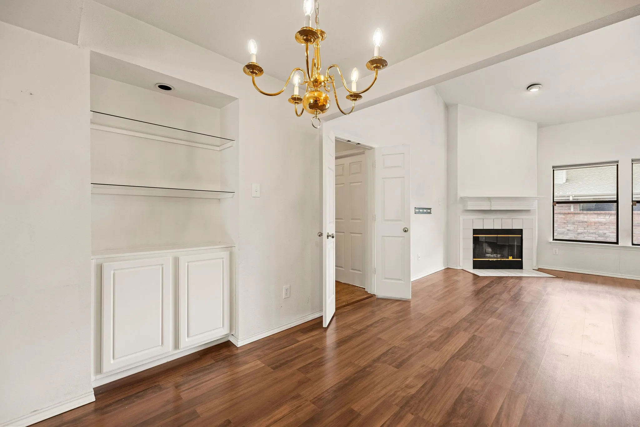 Unfurnished living room with wood finished floors, a chandelier, a tiled fireplace, and baseboards