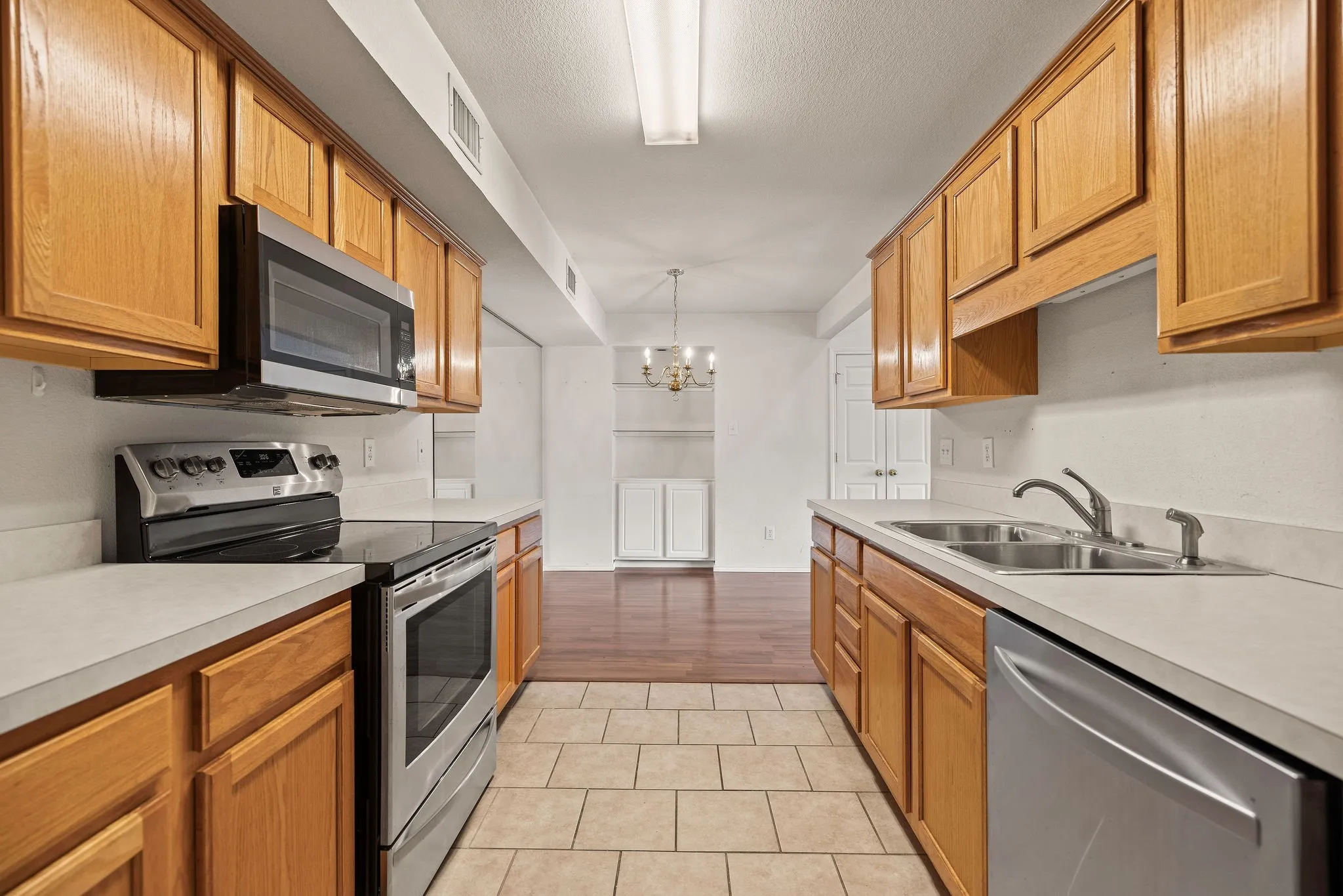 Kitchen featuring stainless steel appliances, light countertops, a sink, a chandelier, and light tile patterned floors