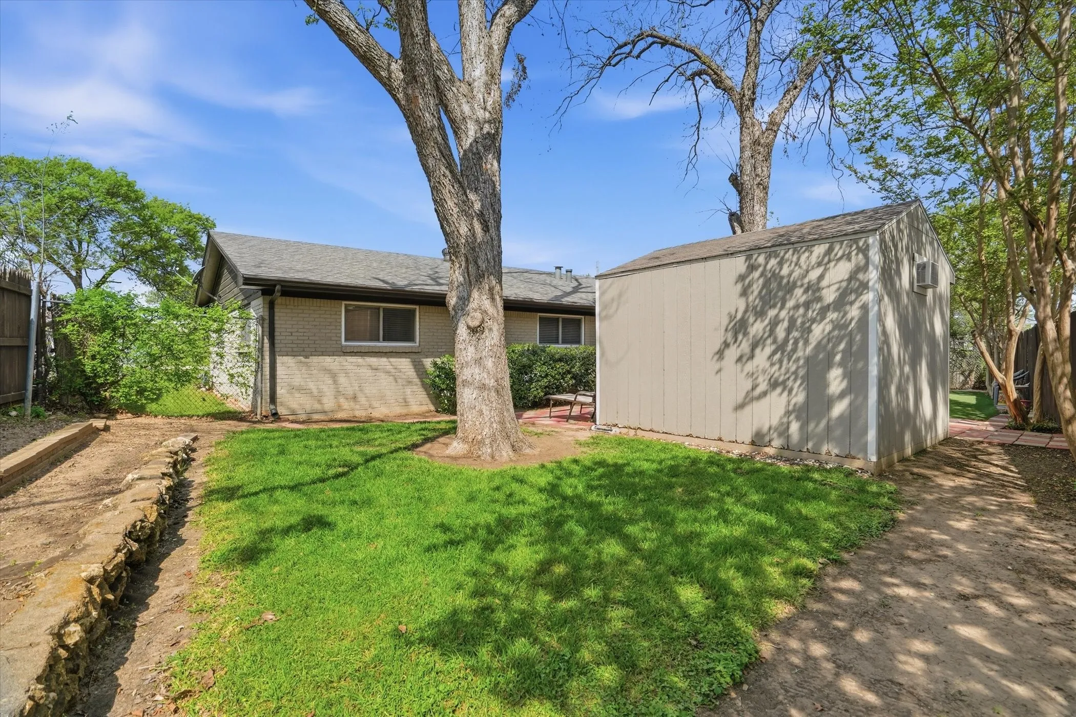 Rear view of house featuring brick siding, a storage unit, and a patio area