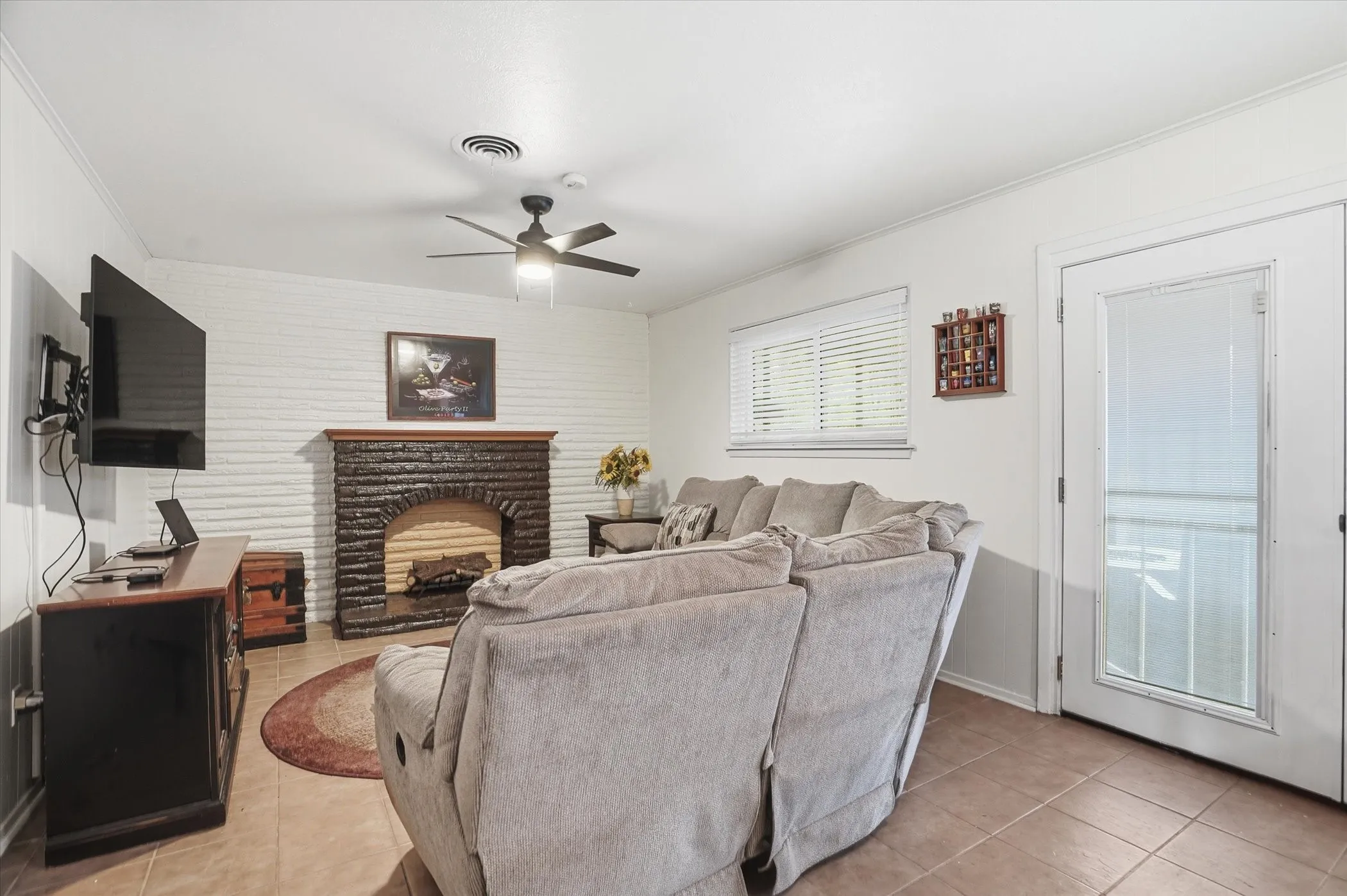 Living room featuring crown molding, a fireplace, ceiling fan, and light tile patterned floors