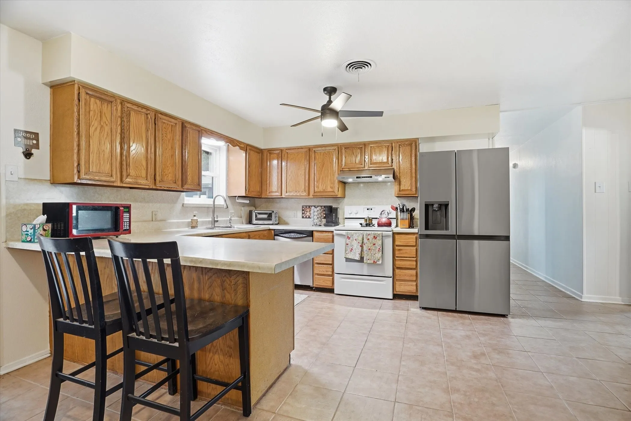 Kitchen featuring light countertops, stainless steel appliances, a ceiling fan, a peninsula, and wood finish cabinets
