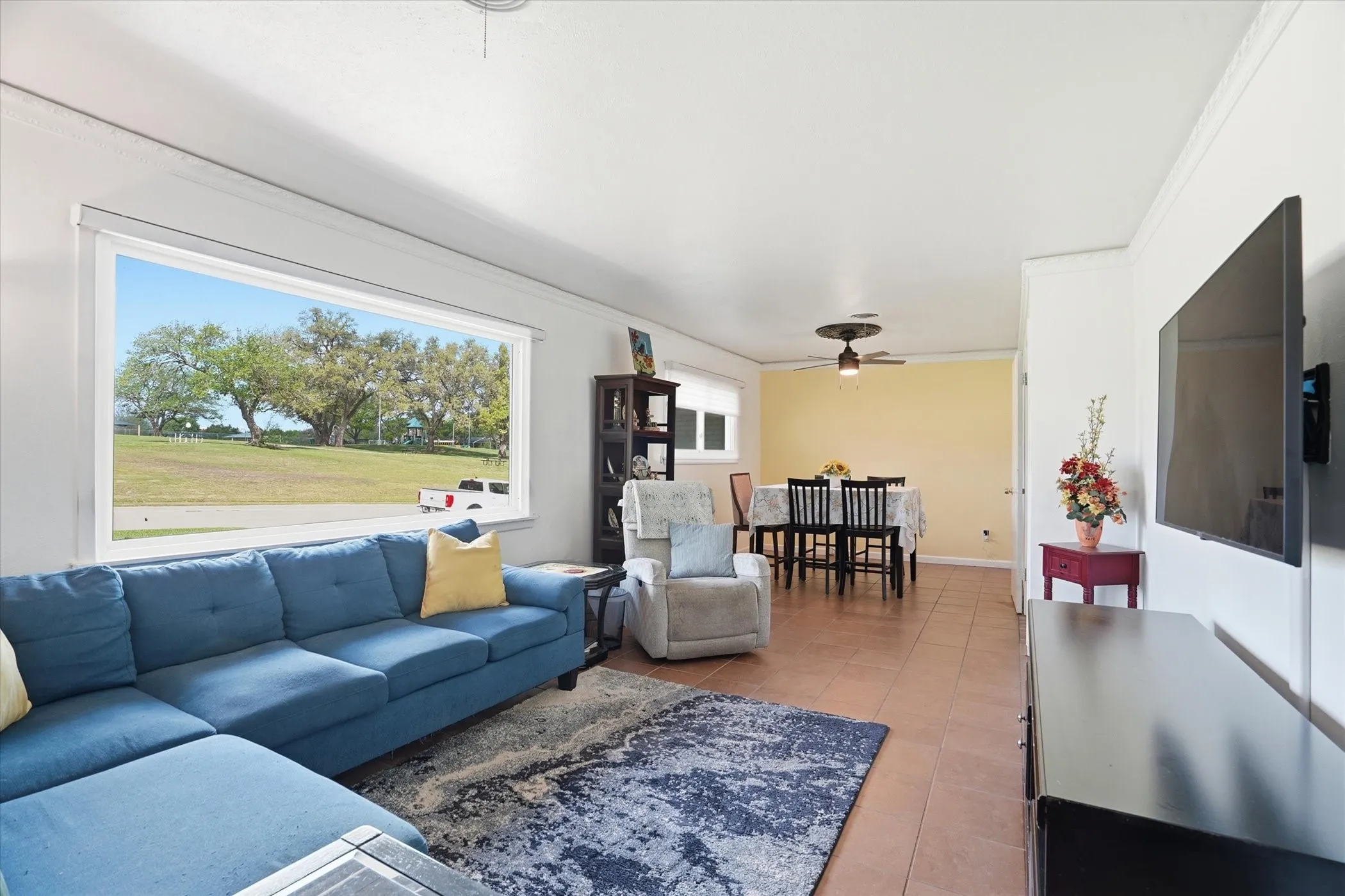 Living room featuring ceiling fan, crown molding, and light tile patterned floors