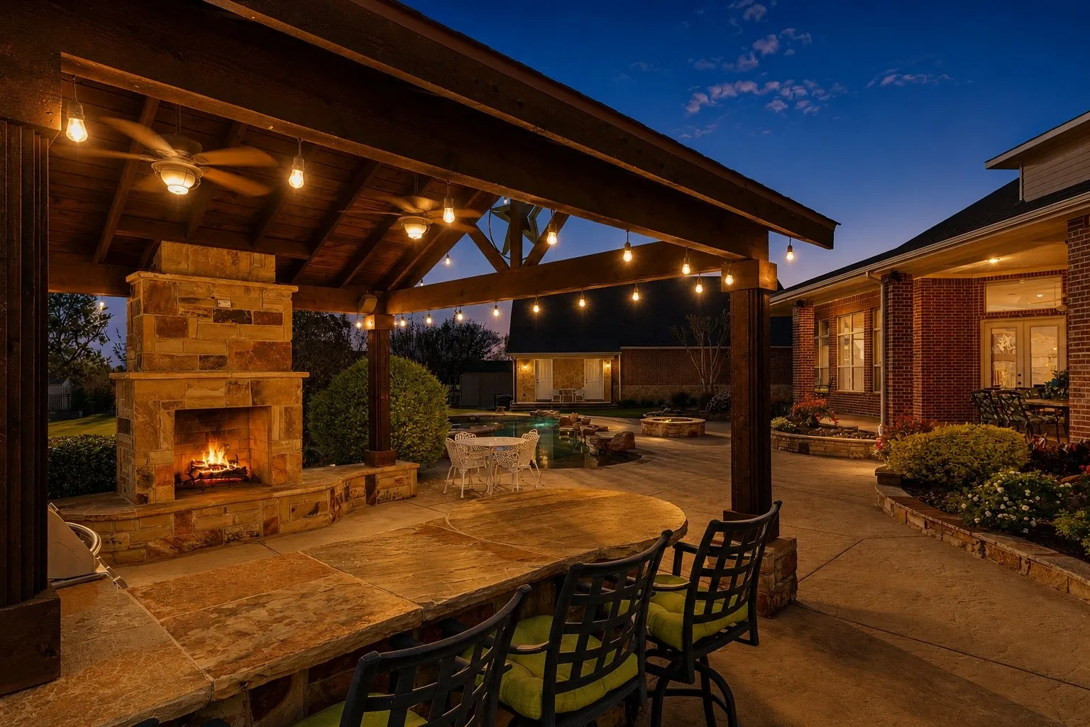 Covered outdoor living space featuring a stone fireplace, wood-beamed ceiling, ceiling fans, string lighting, and a built-in stone bar
