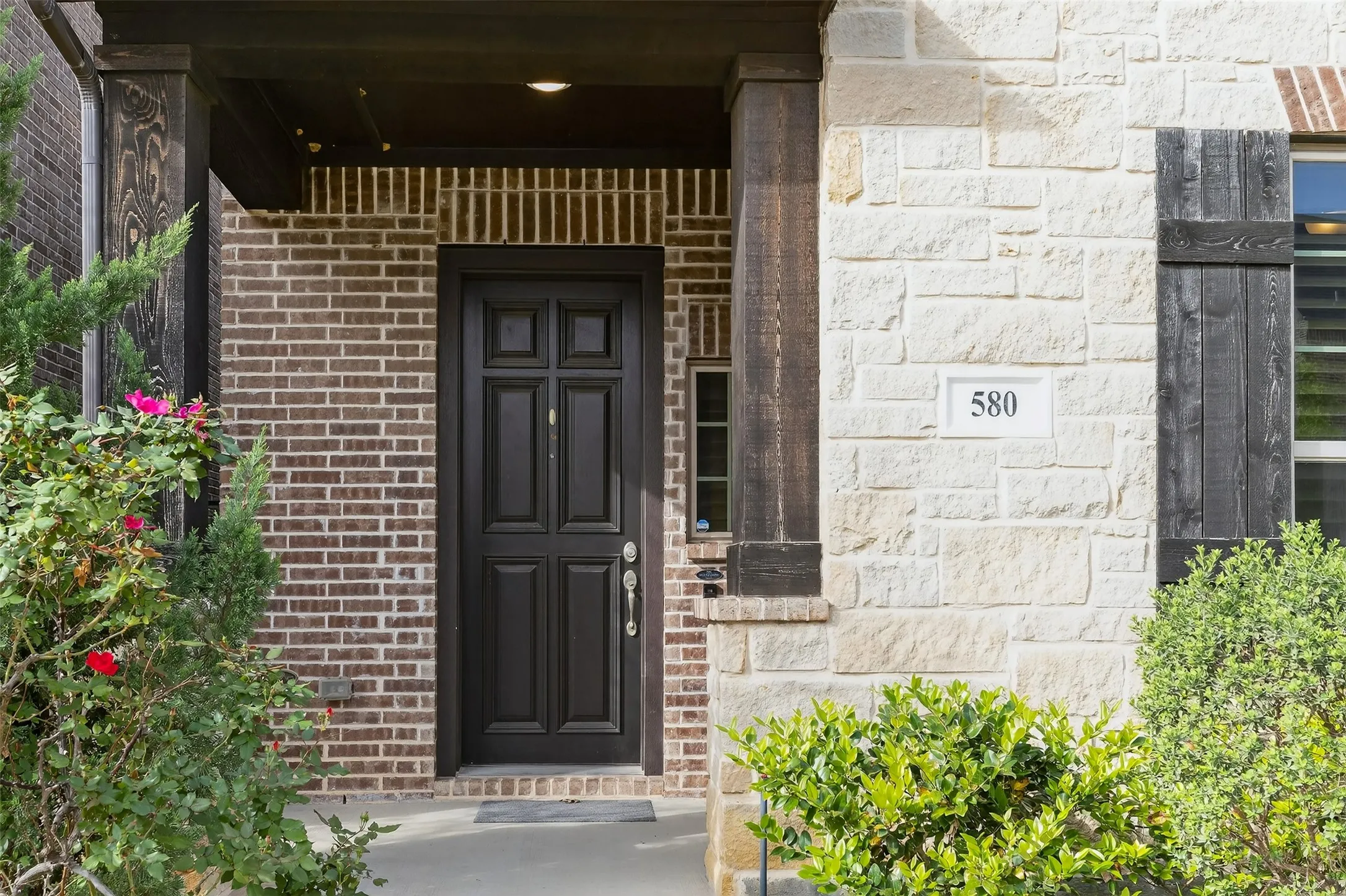 View of exterior entry featuring brick siding, covered porch, and stone siding