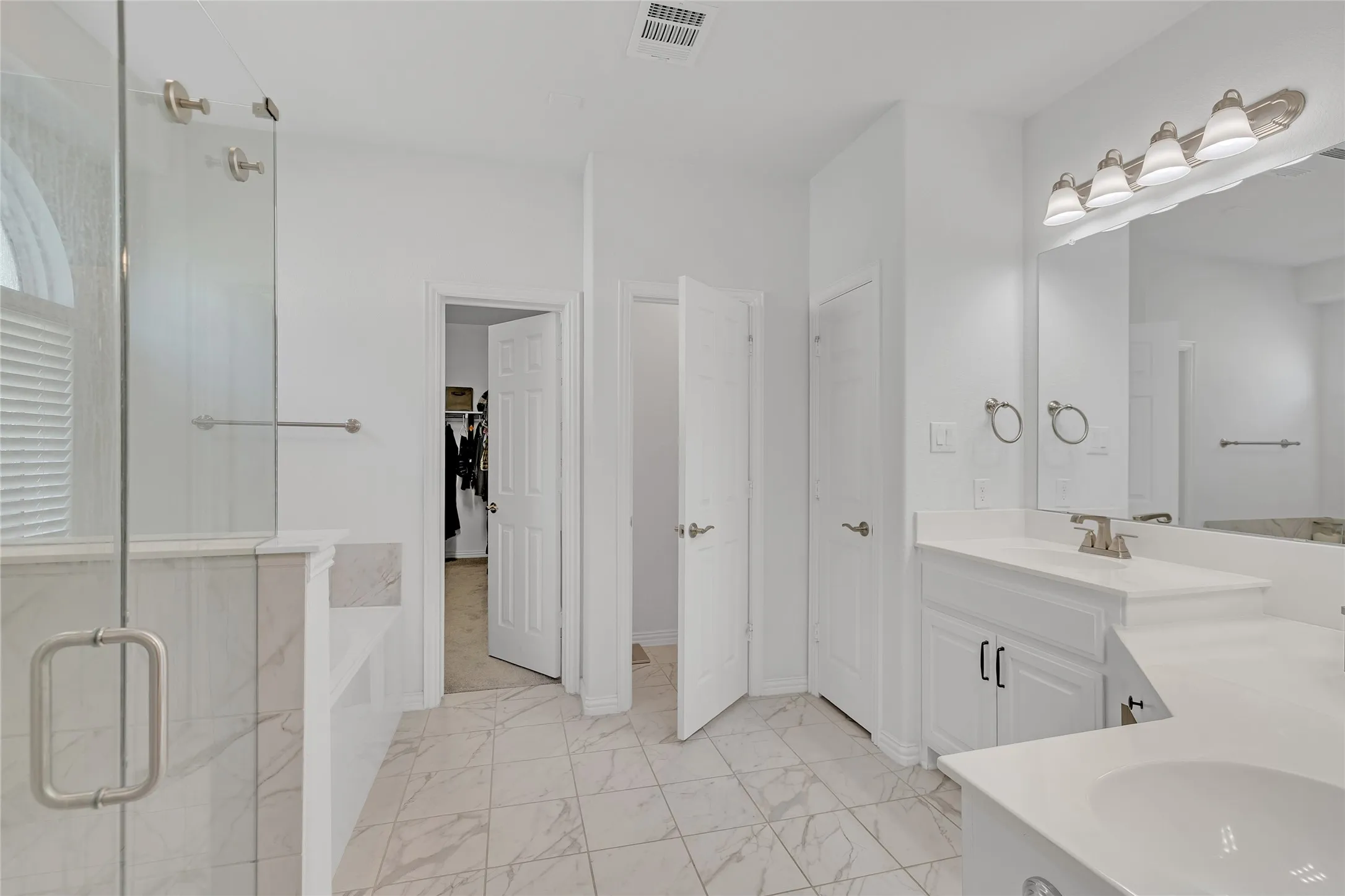 Primary bath with dual sinks, a garden tub, and walk-in shower with glass surround. Door to toilet room, linen storage, and walk-in closet.