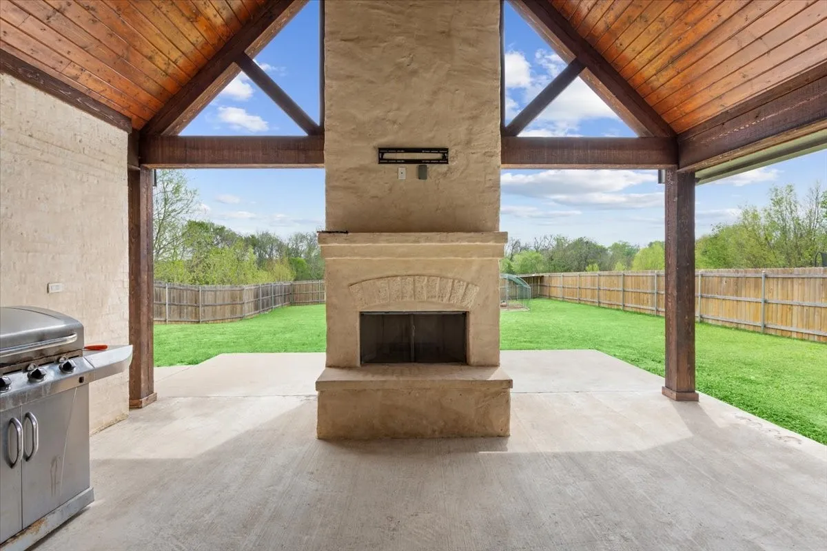 Fenced backyard featuring a fireplace, a patio, and a grill