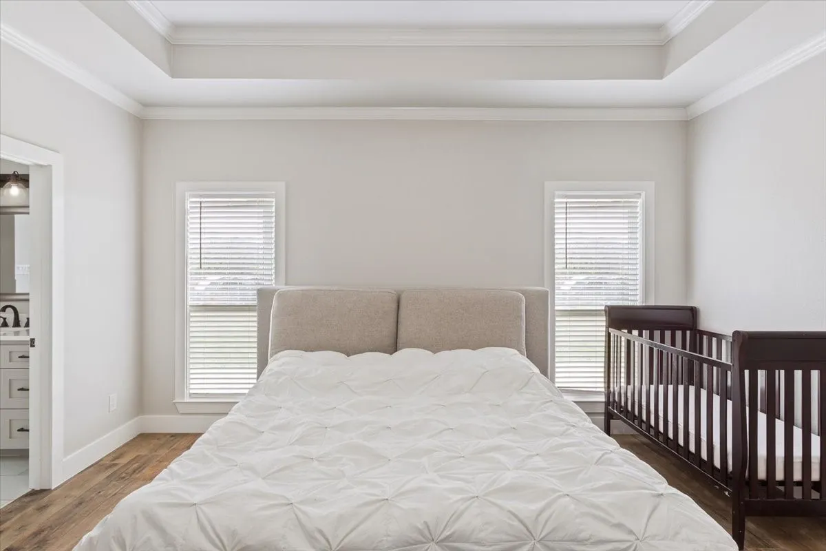 Bedroom with wood finished floors, ensuite bath, and ornamental molding