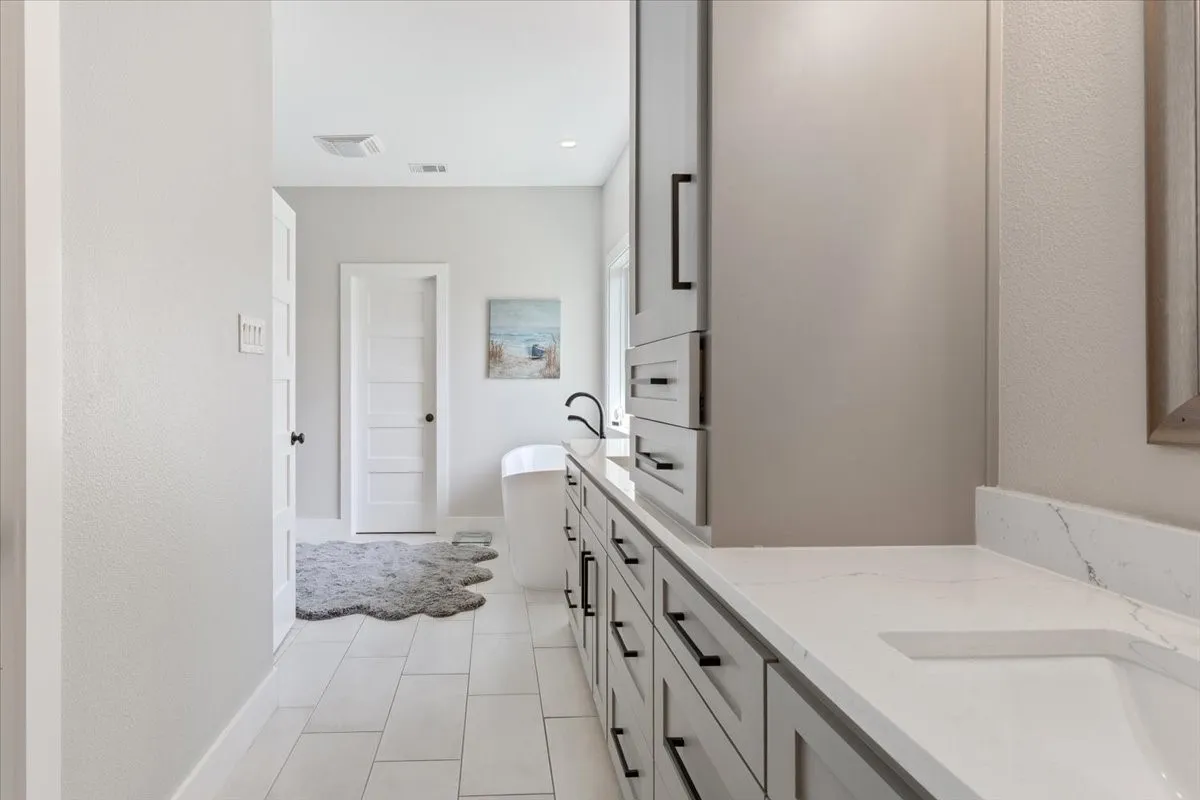 Full bathroom featuring double vanity, a soaking tub, a textured wall, and light tile patterned floors