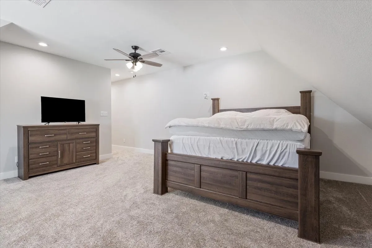 Bedroom with light colored carpet, ceiling fan, lofted ceiling, and recessed lighting
