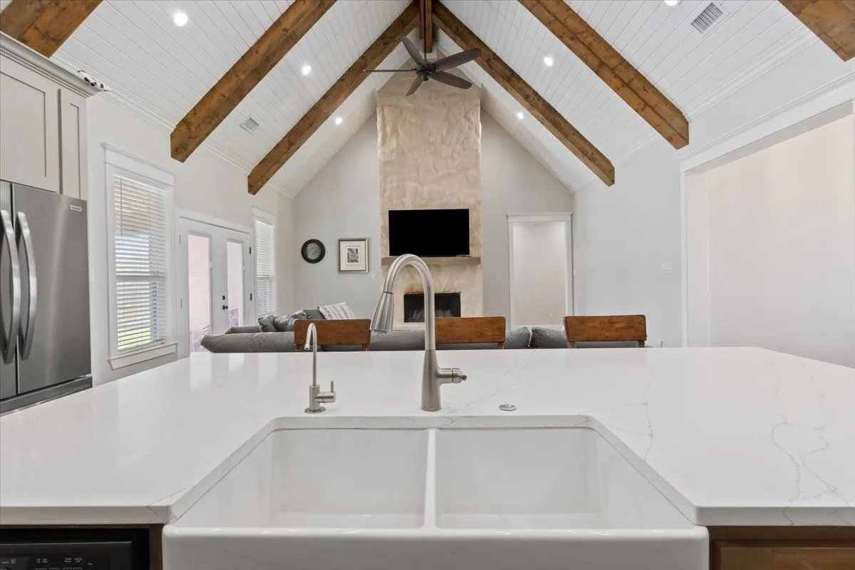 Kitchen featuring open floor plan, a center island with sink, freestanding refrigerator, light stone counters, and ceiling fan