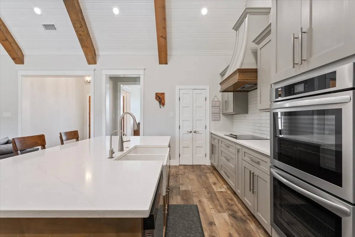 Kitchen featuring double oven, a kitchen island with sink, light stone countertops, a breakfast bar, and decorative backsplash