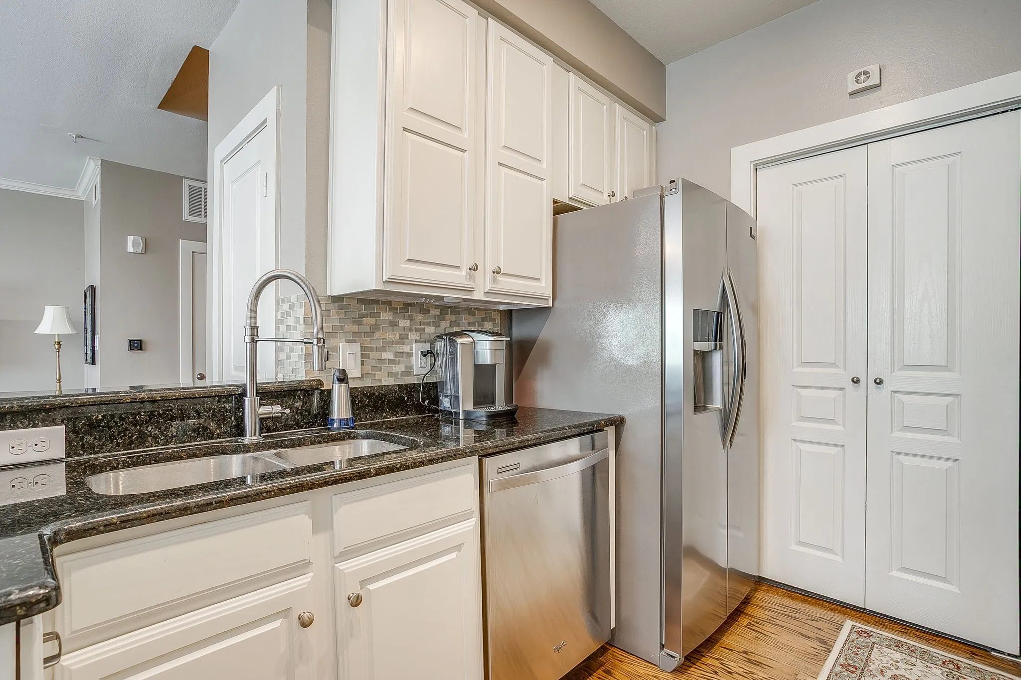 Kitchen featuring dark stone counters, stainless steel appliances, decorative backsplash, white cabinets, and light wood-type flooring