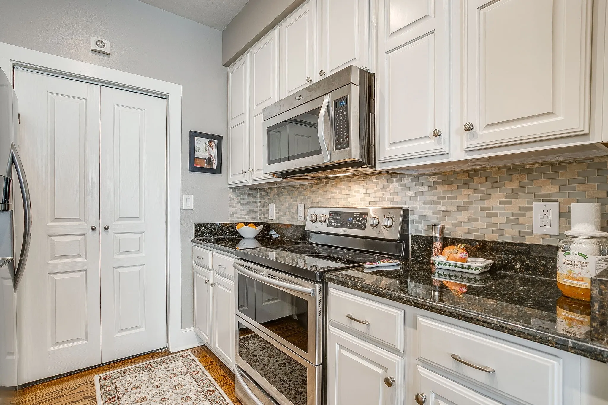 Kitchen with stainless steel appliances, white cabinets, light wood-type flooring, and backsplash