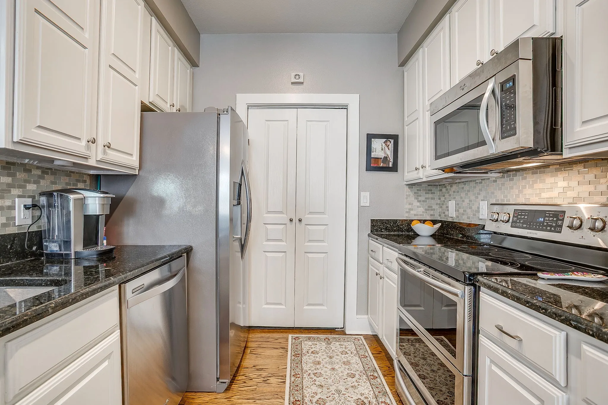 Kitchen with tasteful backsplash, stainless steel appliances, dark stone countertops, and white cabinetry