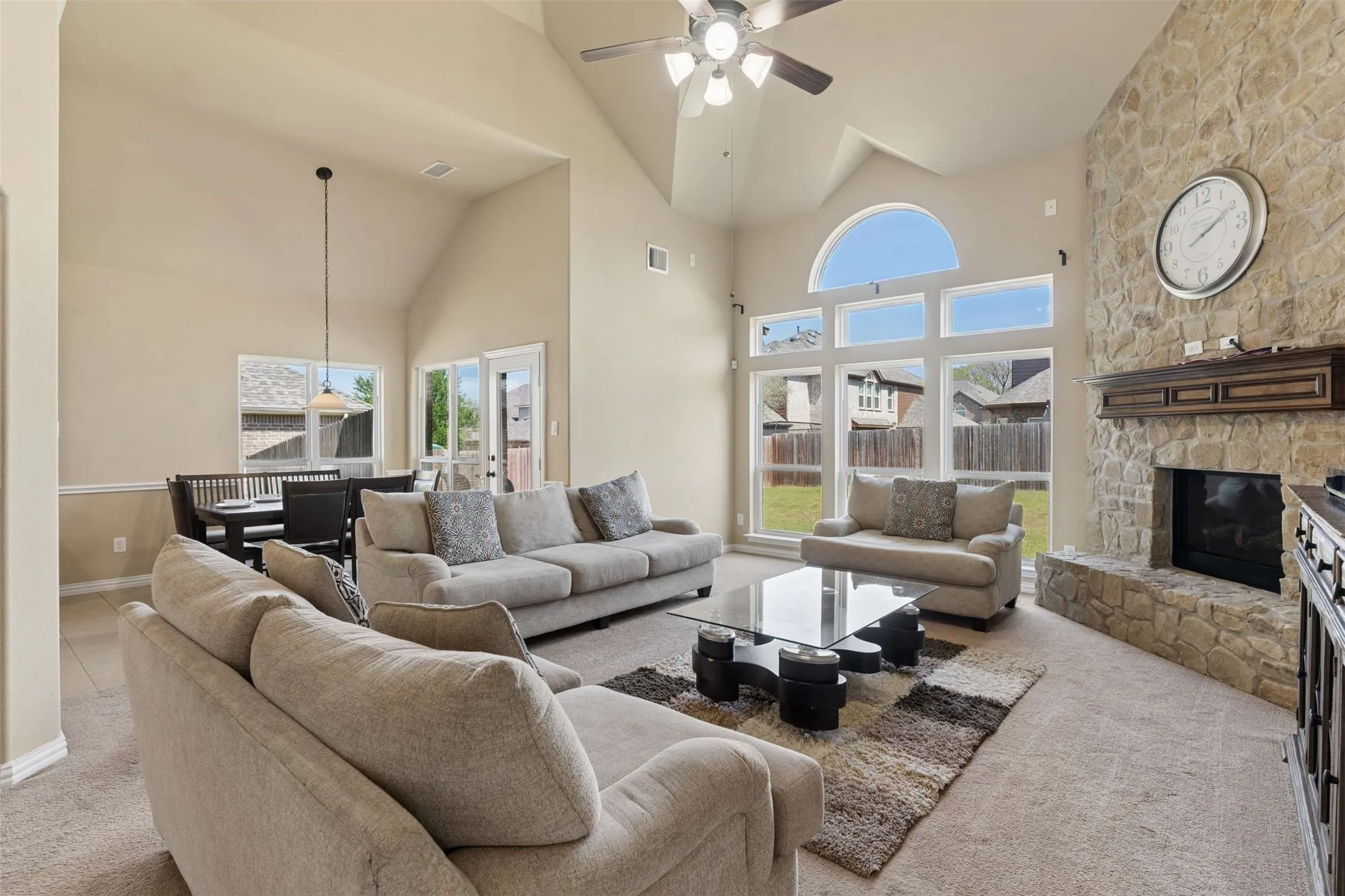 Living room featuring light carpet, a stone fireplace, ceiling fan, and vaulted ceiling
