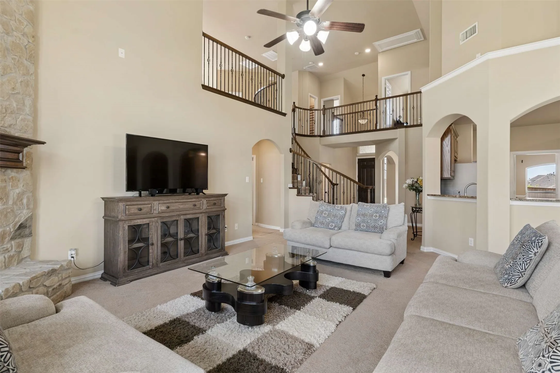 Living area with a ceiling fan, arched walkways, carpet flooring, a high ceiling, and a stone fireplace