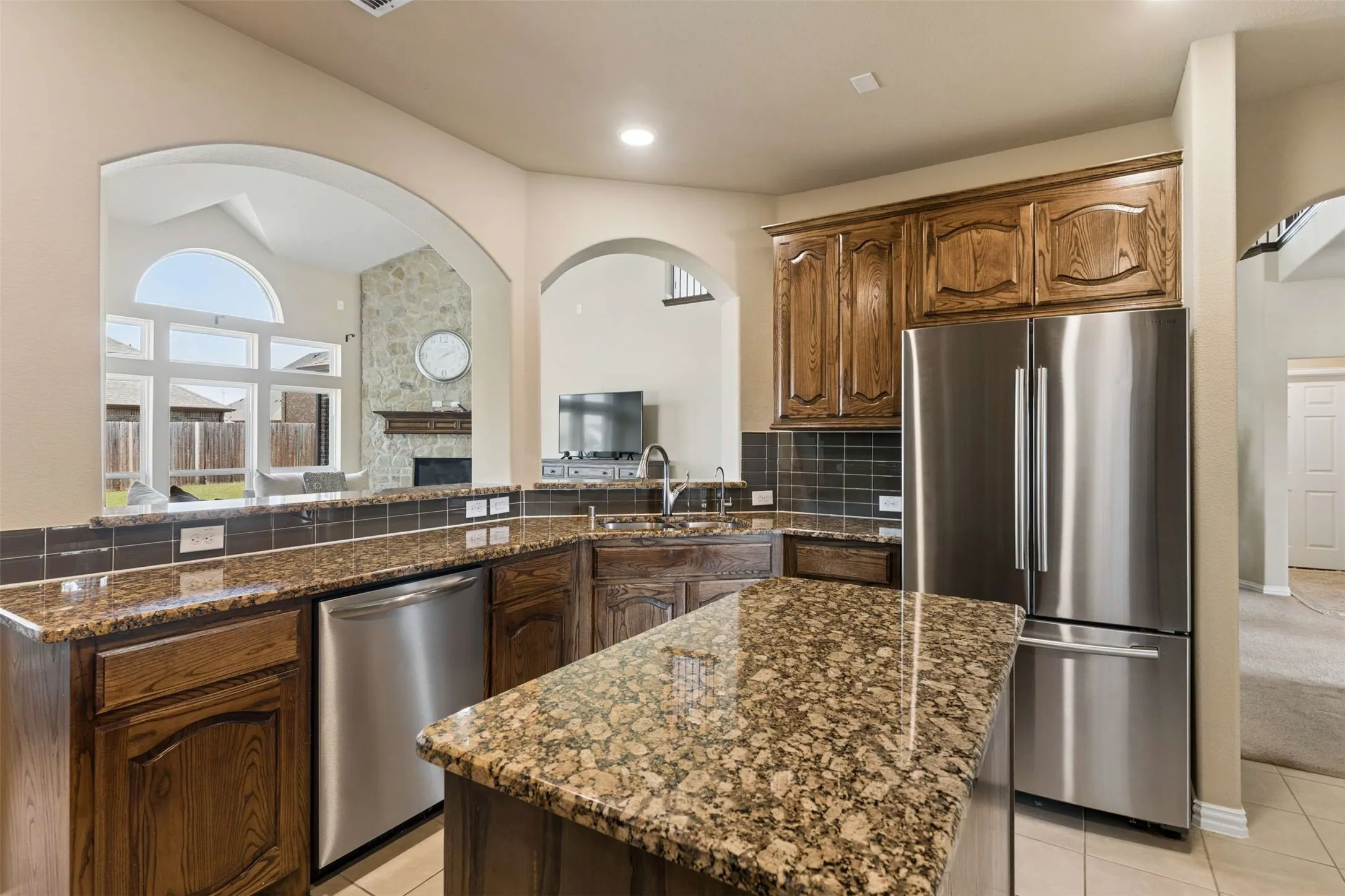 Kitchen with stainless steel appliances, dark stone countertops, a fireplace, backsplash, and light tile patterned flooring